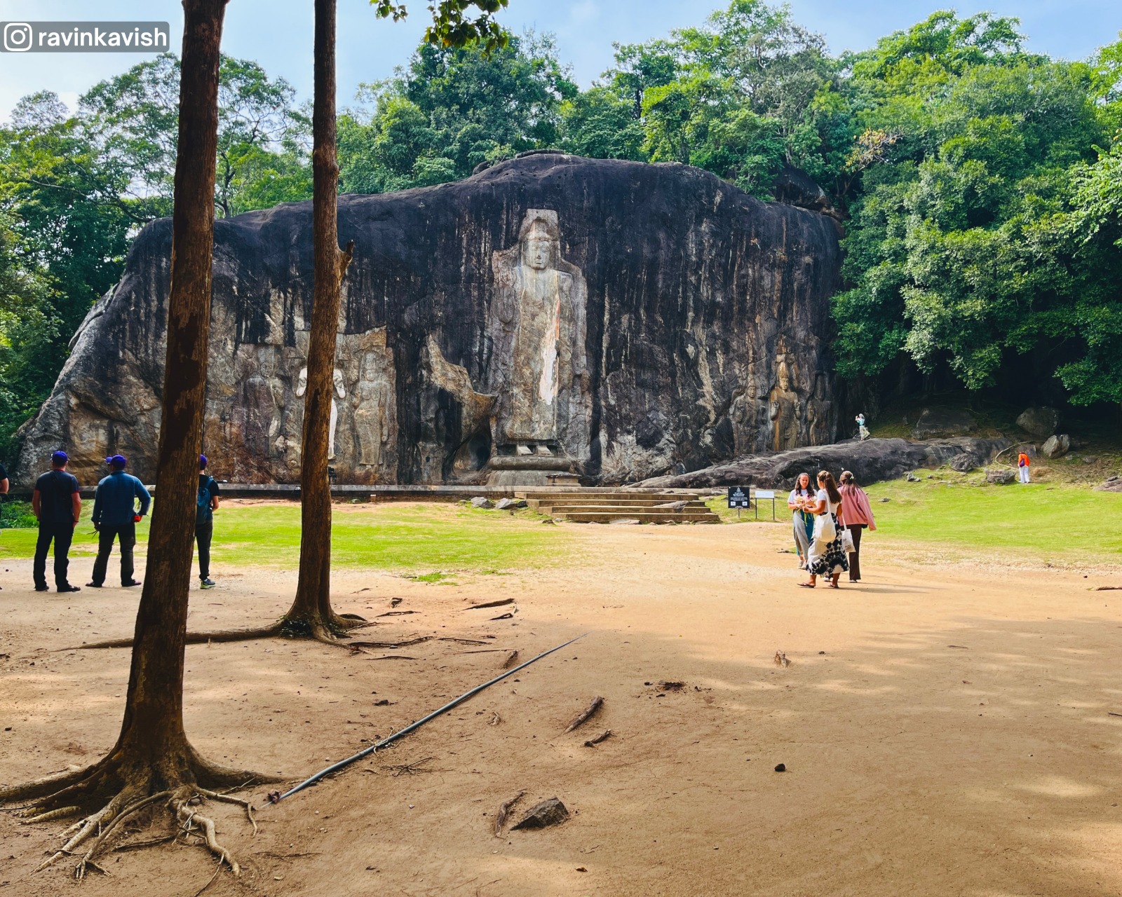 Entire rock face of Buduruwagala Rock Temple with all carvings visible through trees from the end of the pathway showcasing Sri Lankas cultural heritage