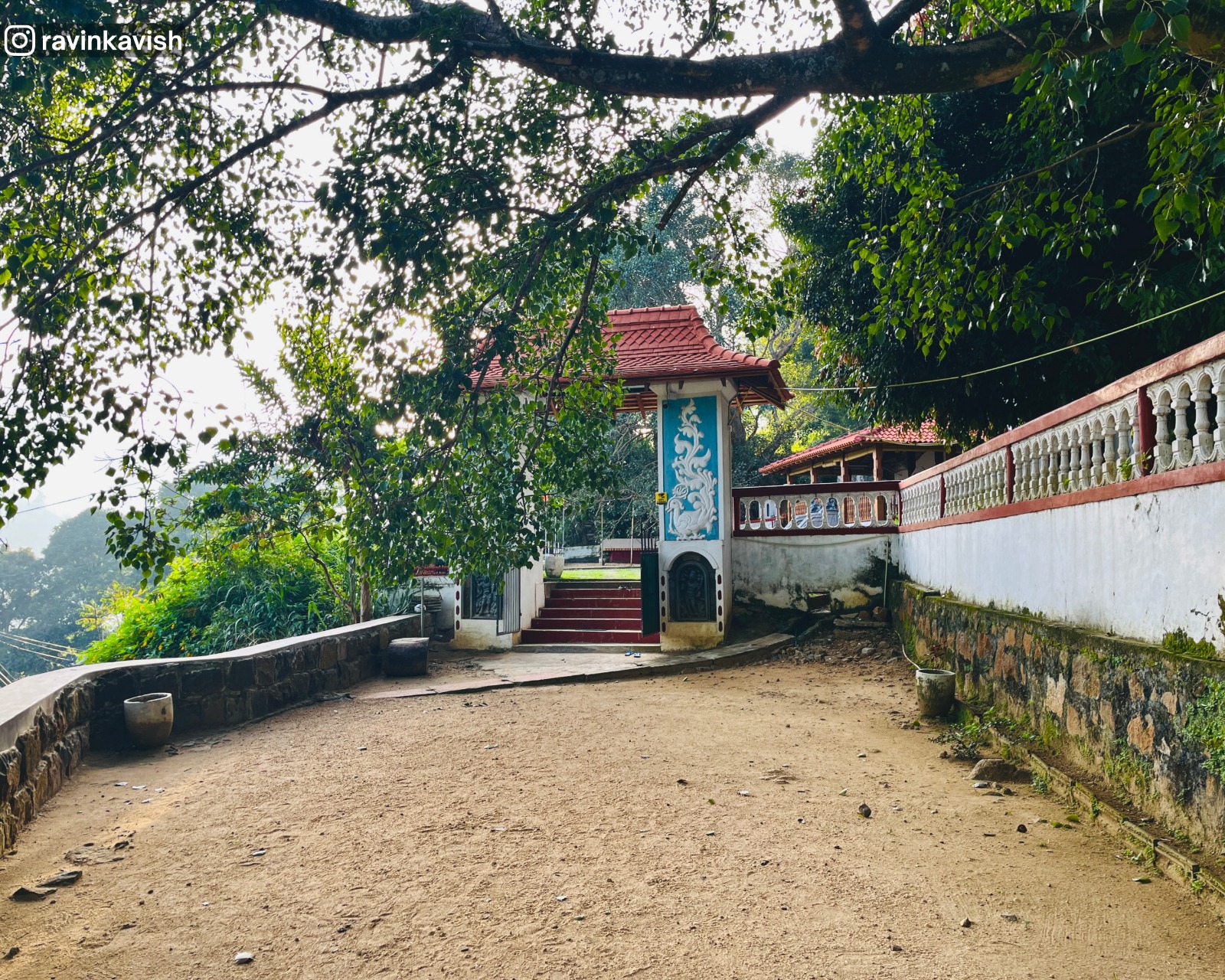 Entrance of Ravana Royal Temple, near Ella, viewed from a distance, showing surrounding nature, rocks, and greenery