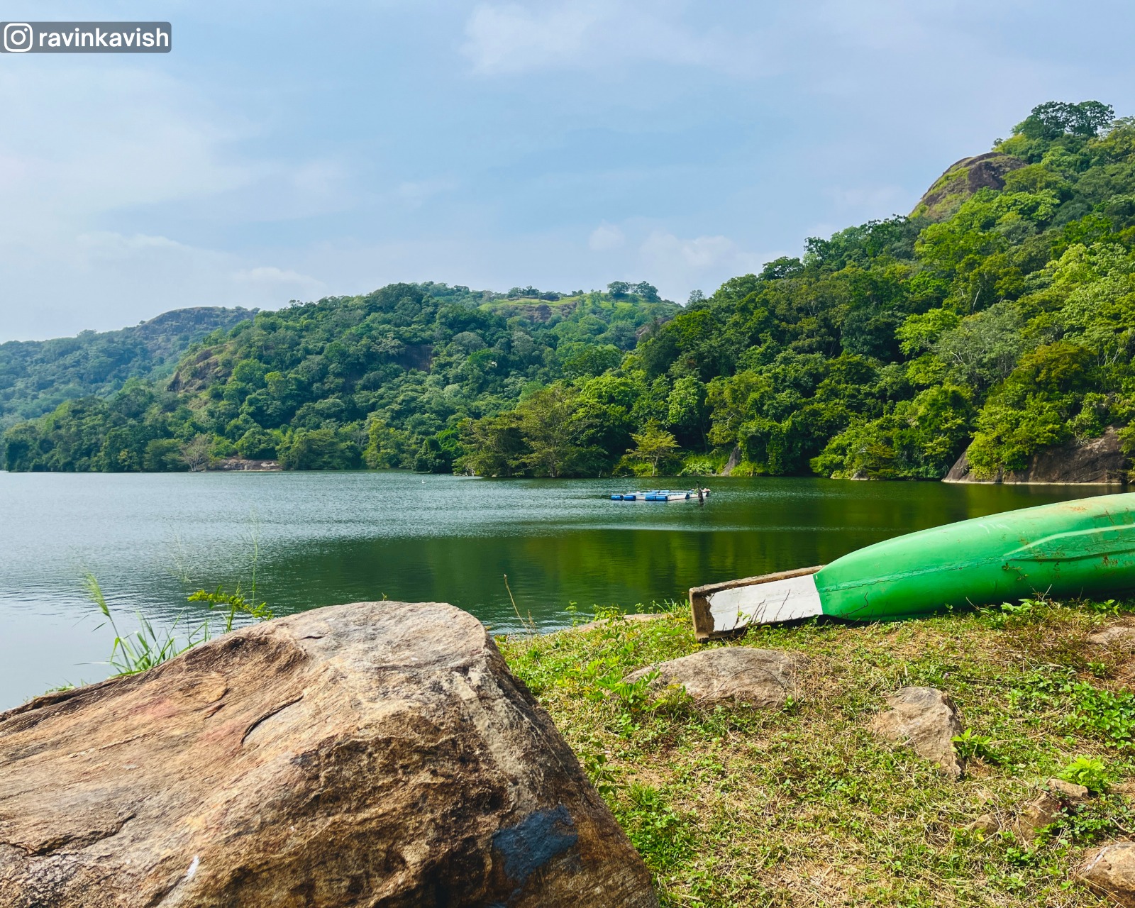 First section of Buduruwagala Reservoir in Ella with surrounding tree-covered hills, a canoe, and a large boulder on the riverbank showcasing Sri Lankas scenic landscapes