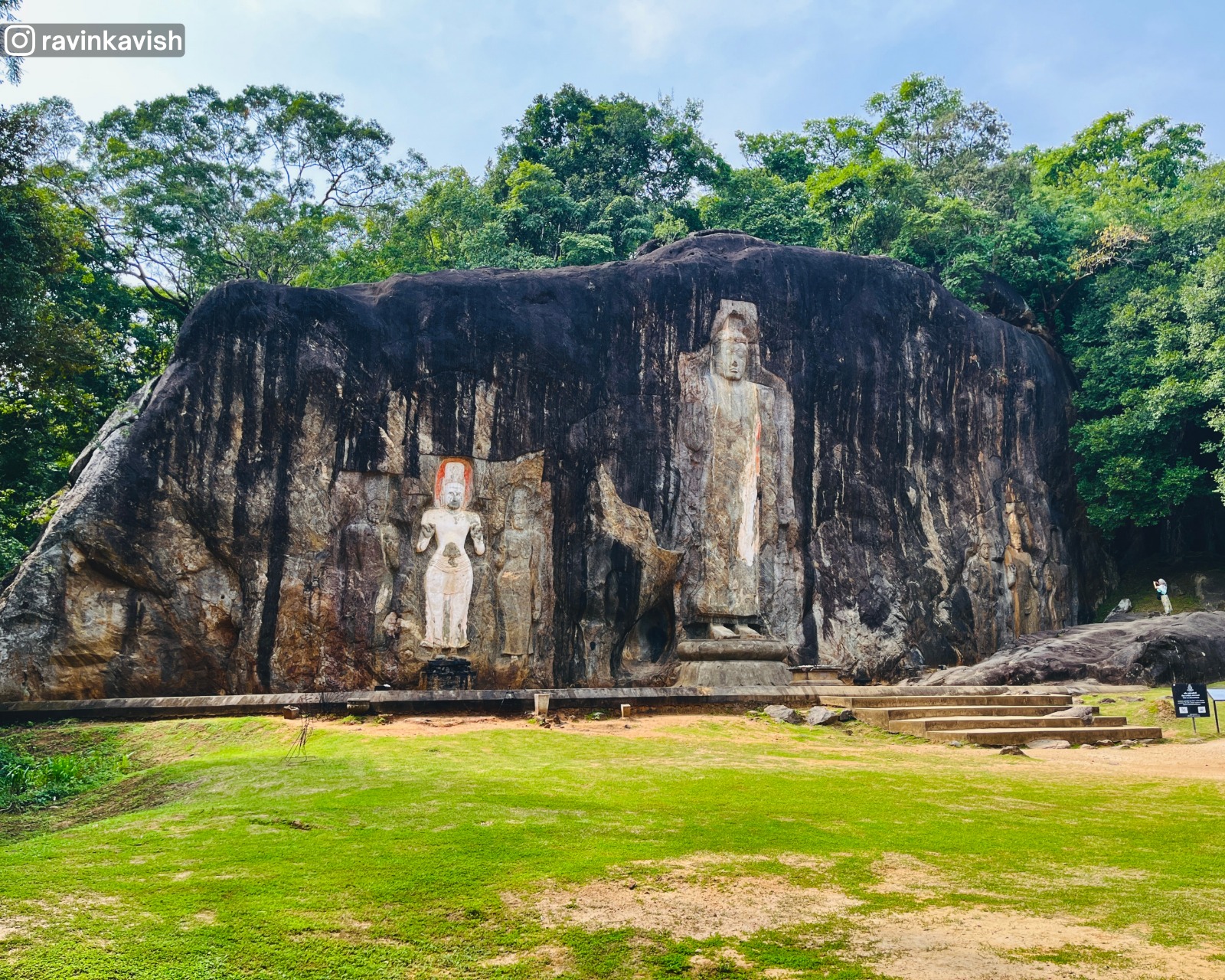 Front view of the entire rock face at Buduruwagala Rock Temple with open grassland in front showcasing Sri Lankas cultural landscape