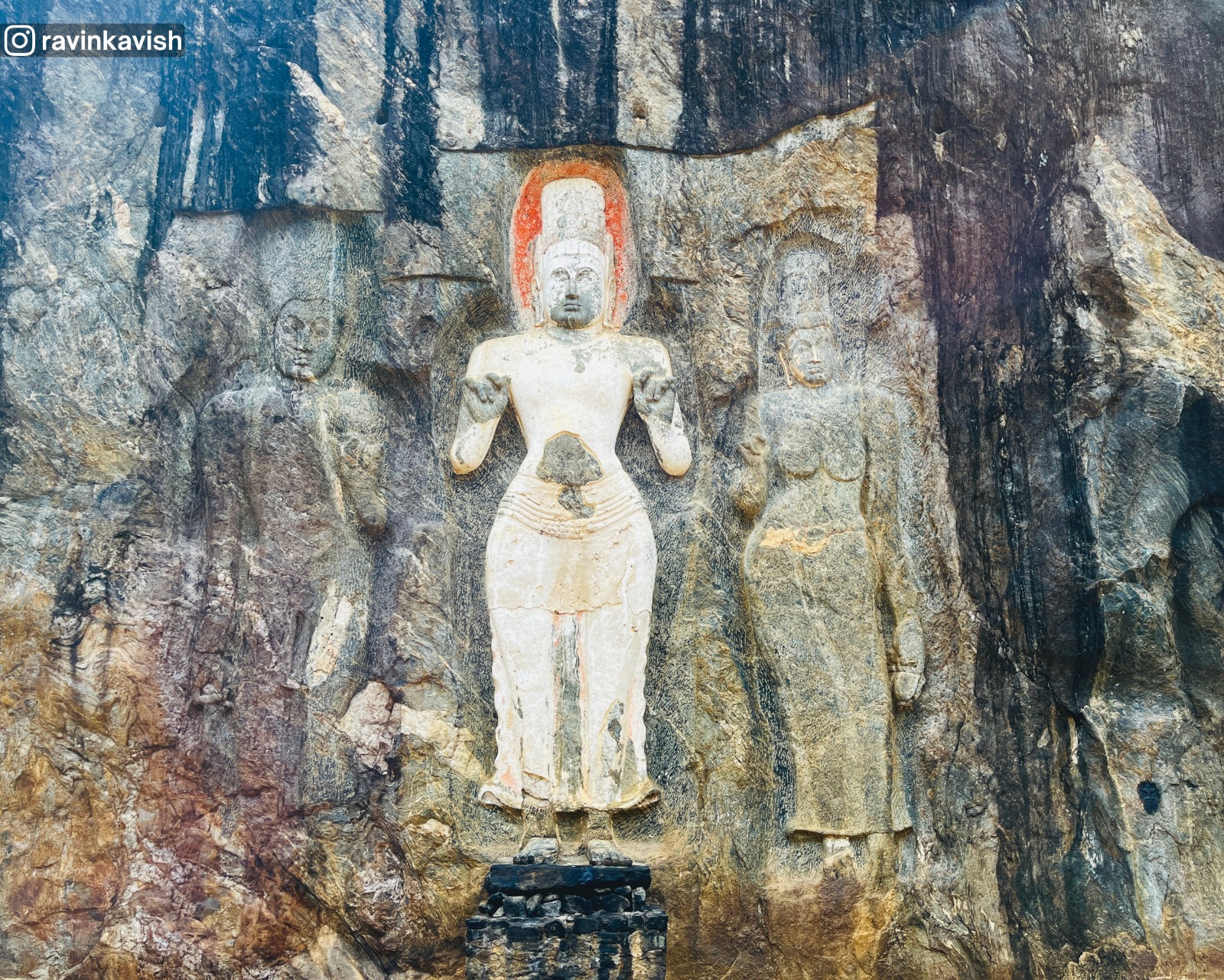Left-side Buduruwagala rock carvings in Ella showing three figures, with the middle figure standing out with a white color and an orange curve on its crown, showcasing Sri Lankas cultural heritage