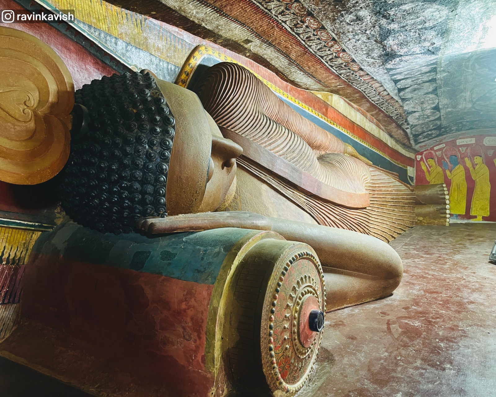Old colorful reclining Buddha at the cave temple of Rakkiththa Kanda Rajamaha Viharaya with surrounding ancient murals and statues