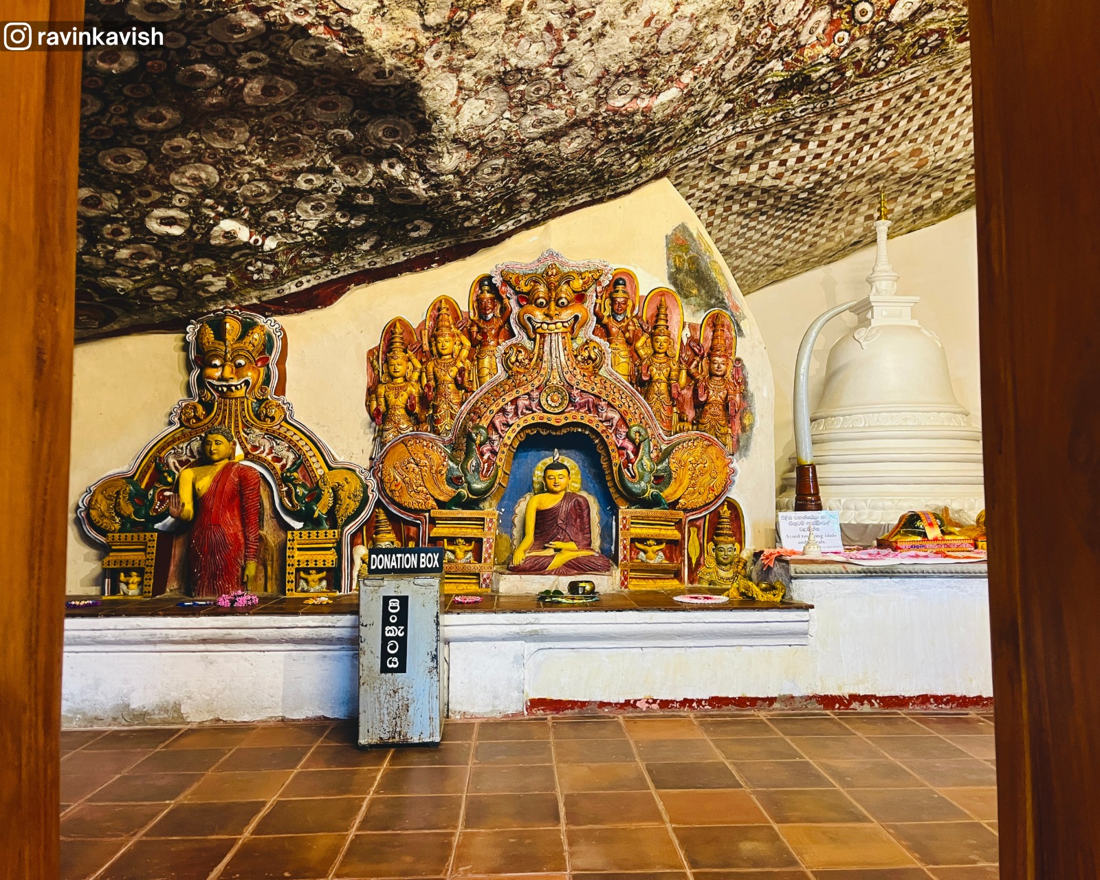 Ravana Royal Cave Temple interior in Ella, Sri Lanka, showing seated and standing Buddhas, god-like figures, a small stupa, and oval-patterned murals