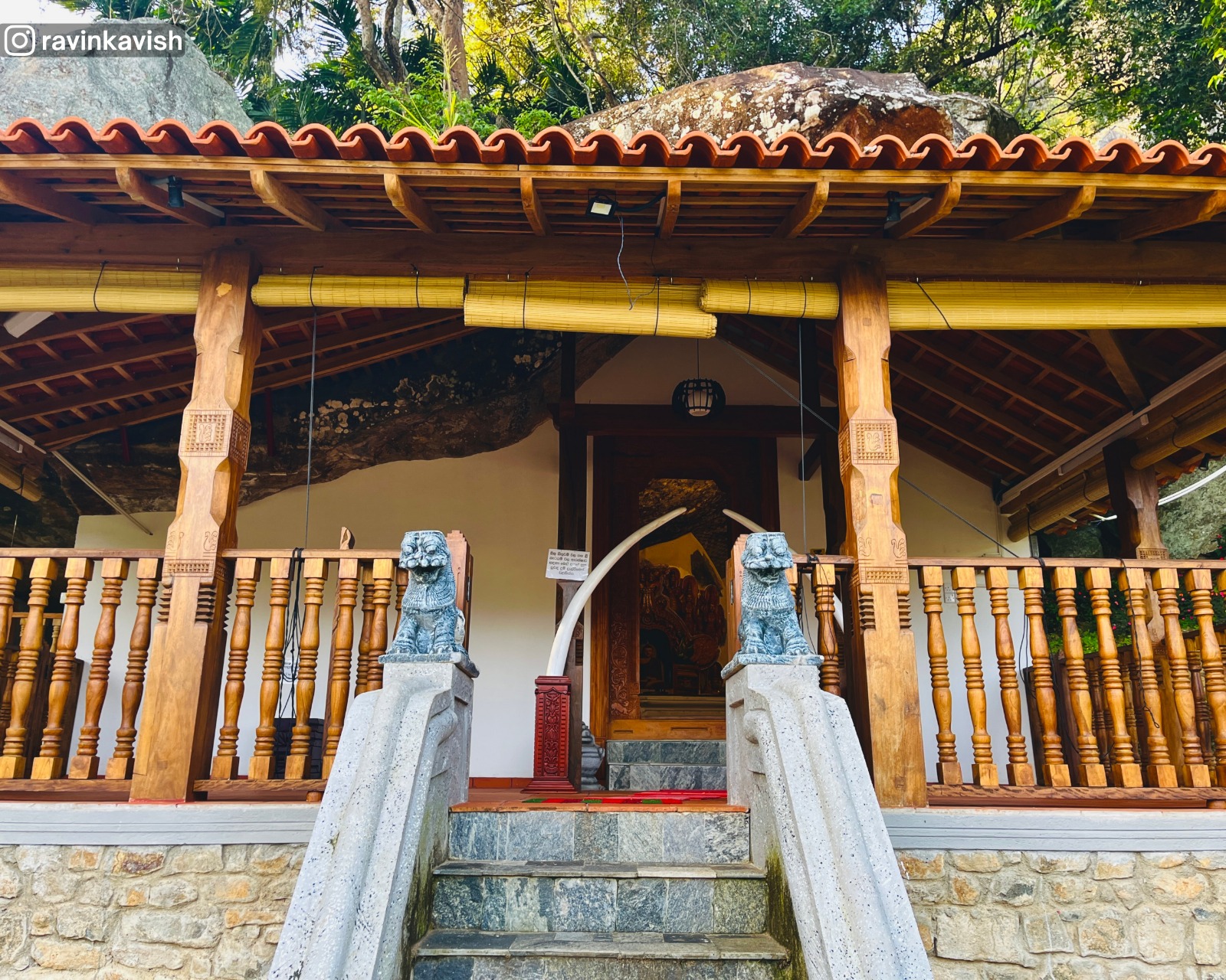 Staircase leading to Ravana Royal Cave Temple in Ella, Sri Lanka, with the wooden entrance, nearby rock formations, and trees
