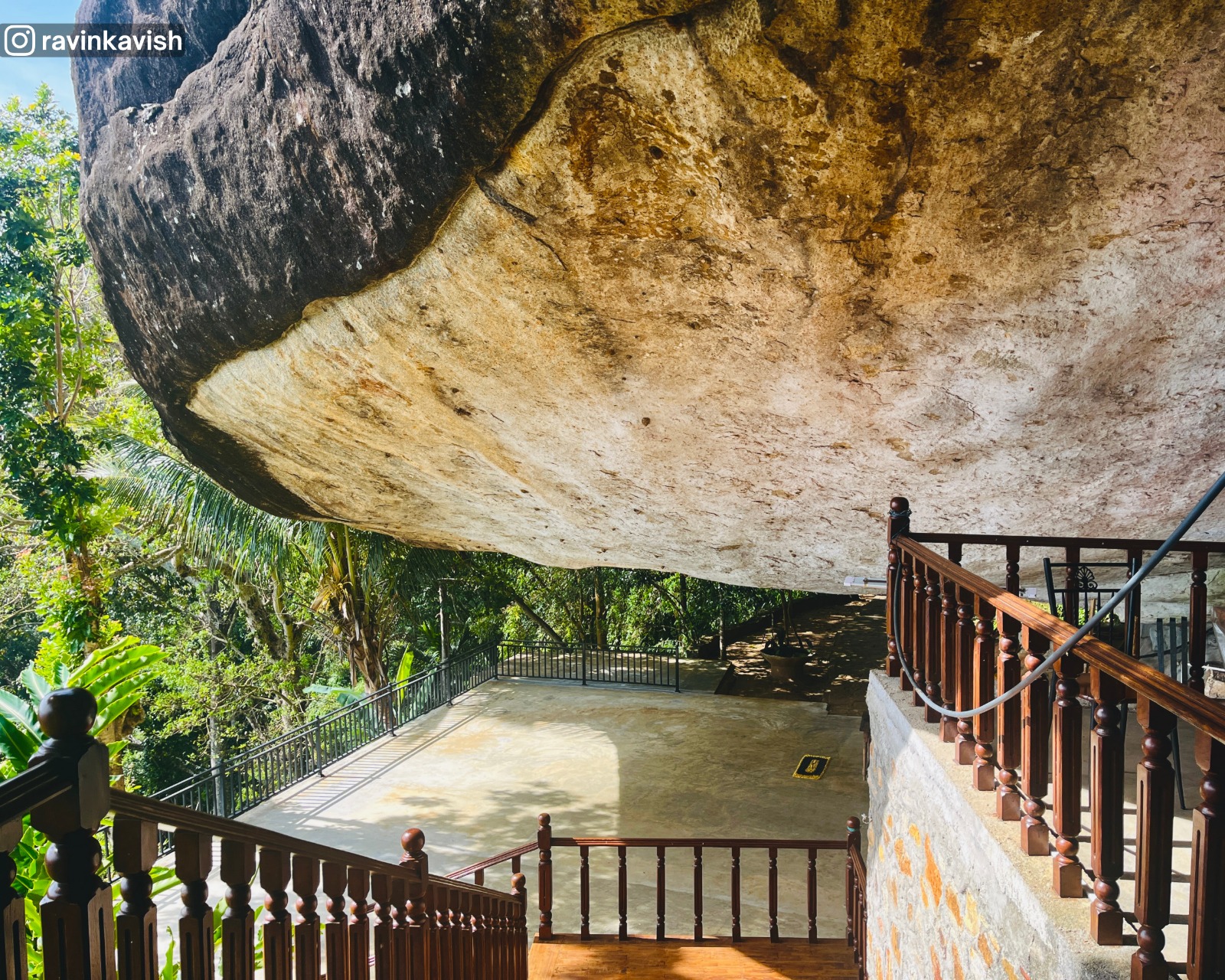 Stone staircase with a fence at Rakkiththa Kanda Rajamaha Viharaya leading up to the rock-sheltered area, showing the view of the surrounding temple area from the steps