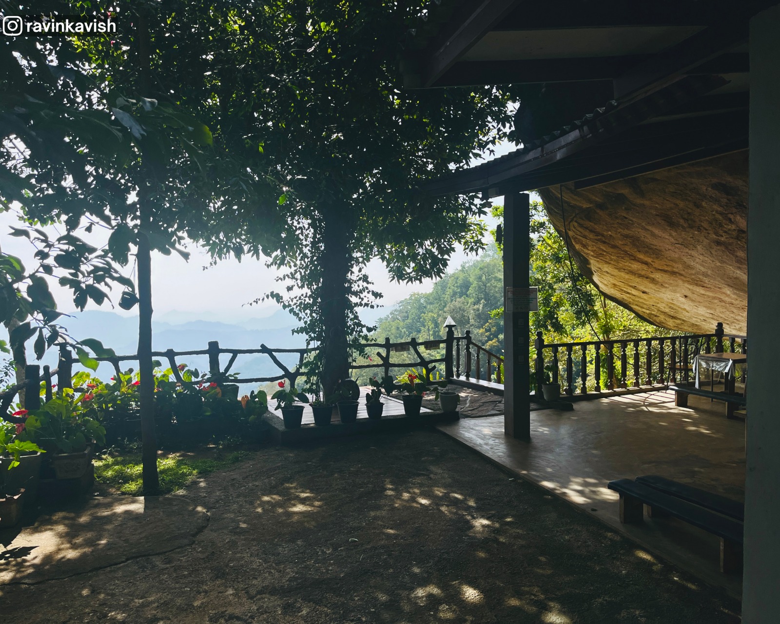 Terrace garden at Rakkiththa Kanda Rajamaha Viharaya with a fence, distant hills and mountains, and a focus on the natural rock shelter roof