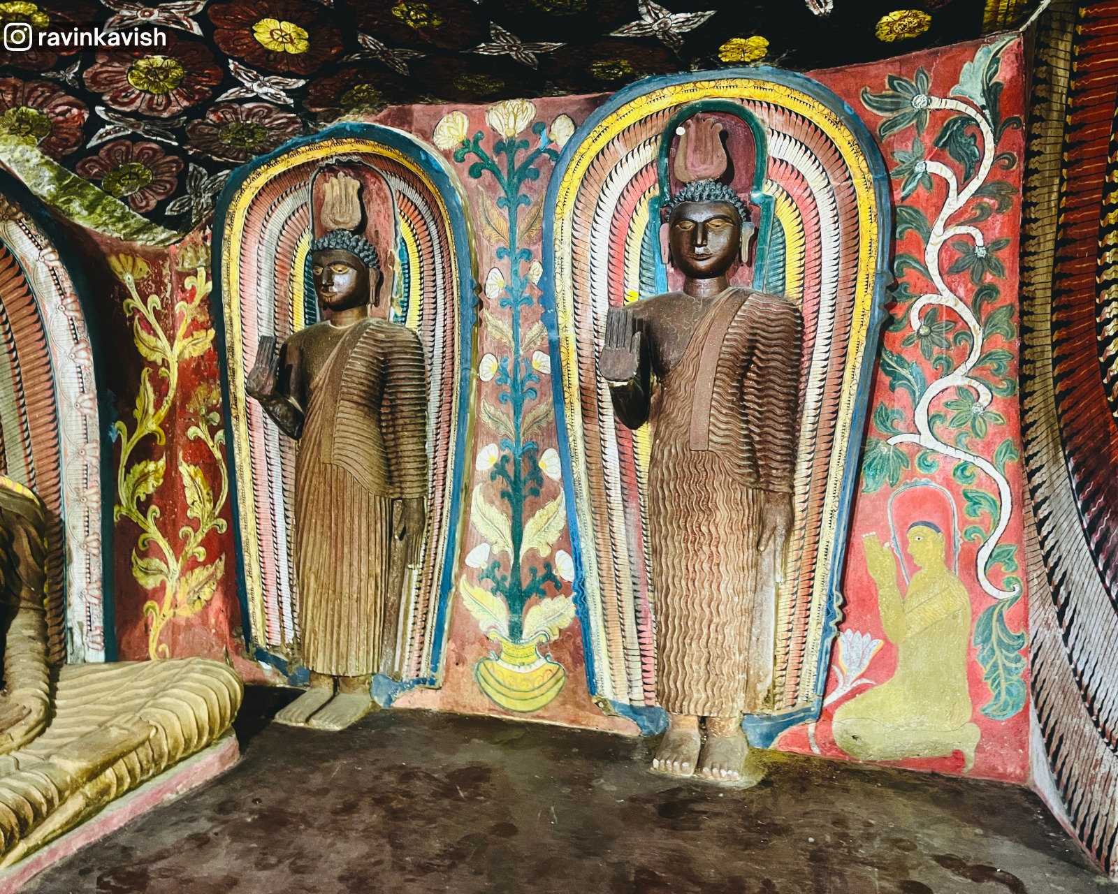 Two old standing Buddha statues at the cave temple of Rakkiththa Kanda Rajamaha Viharaya with surrounding murals and a glimpse of a seated Buddha