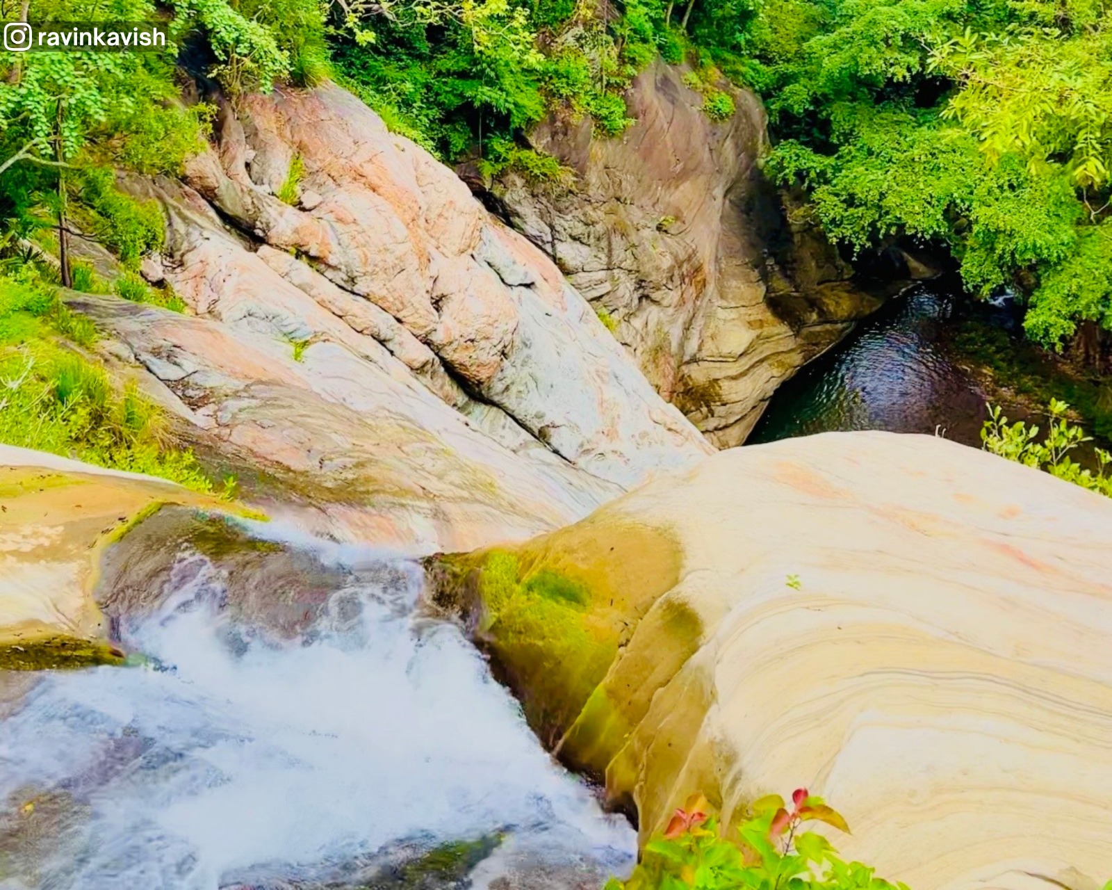 View from the second tier of Pallewela Waterfall looking down to the last basin, showing smooth waterfall rock surfaces and surrounding lush nature