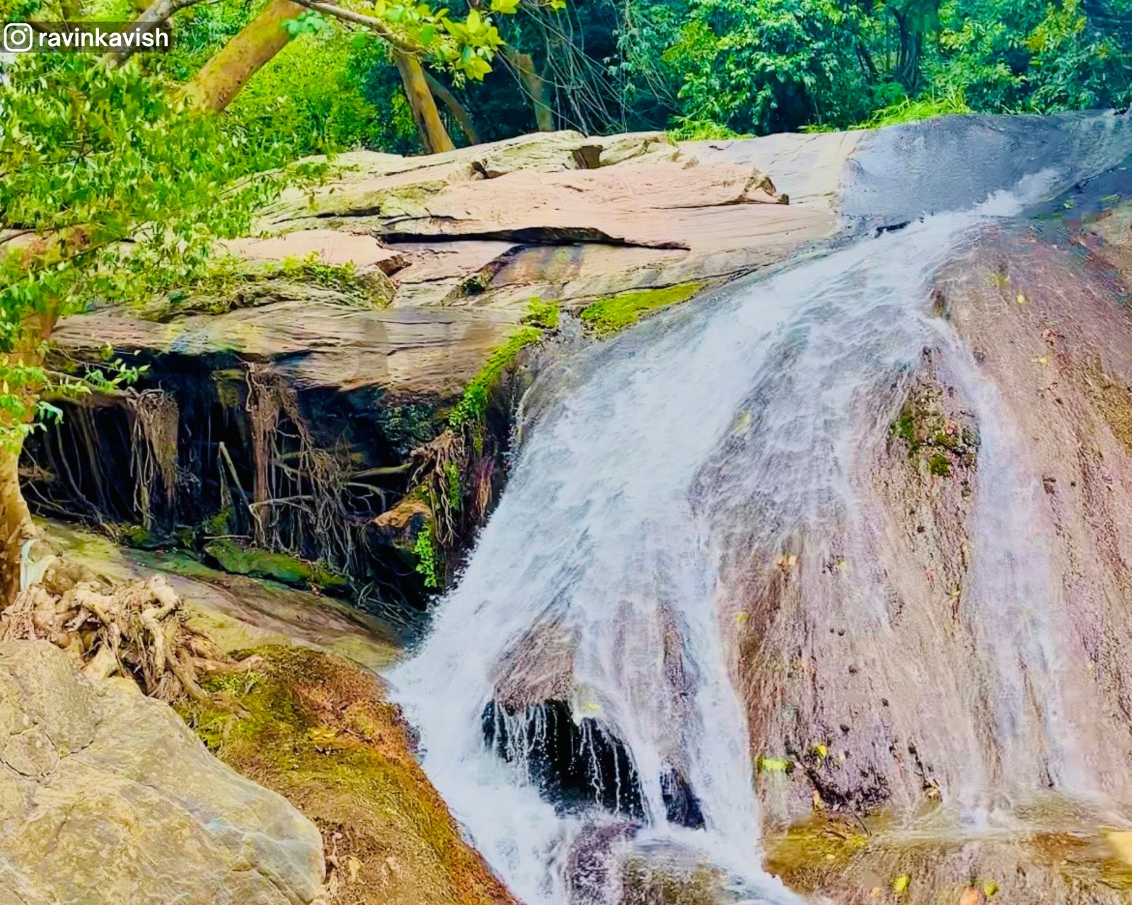 View from the second tier of Pallewela Waterfall showing water cascading over smooth and rough rocks into the last basin