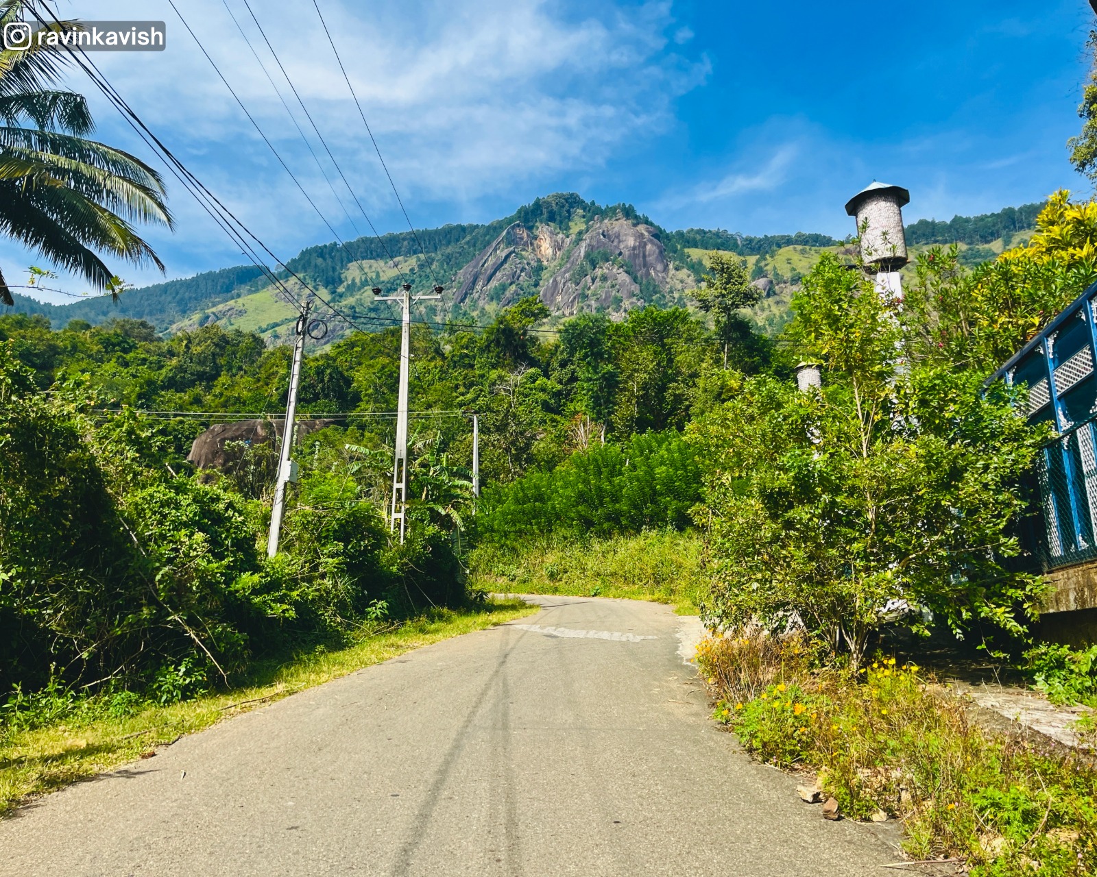 View of Kurullangala mountain ahead from the road leading to Rakkiththa Kanda Rajamaha Viharaya, with surrounding greenery and nearby structures.