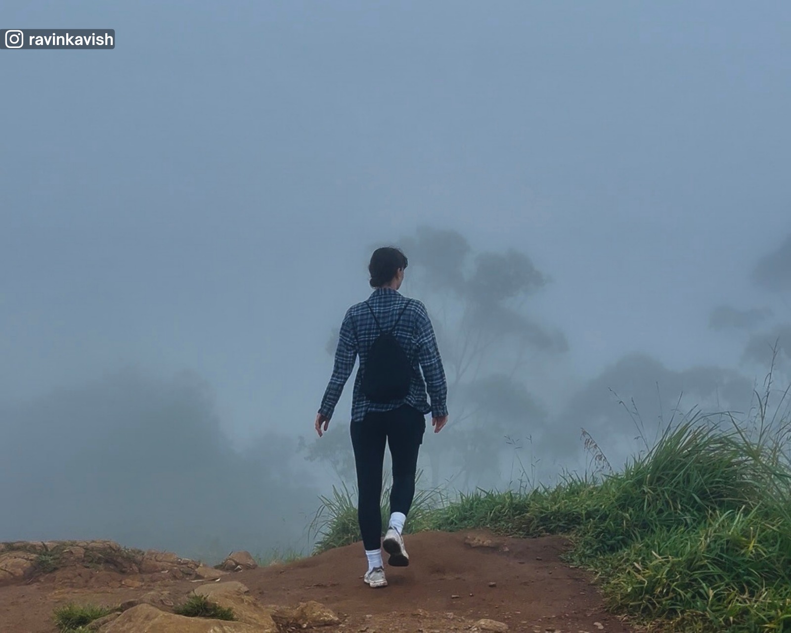 Walk at the summit of Little Adam’s Peak during foggy conditions, showing foreground dirt and grass clearly, with a faint treeline visible in the distance
