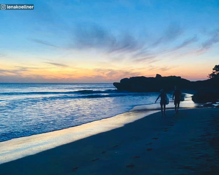 Beach and sea with a rocky outcrop behind two surfers at Maya Beach during sunrise, Sri Lanka