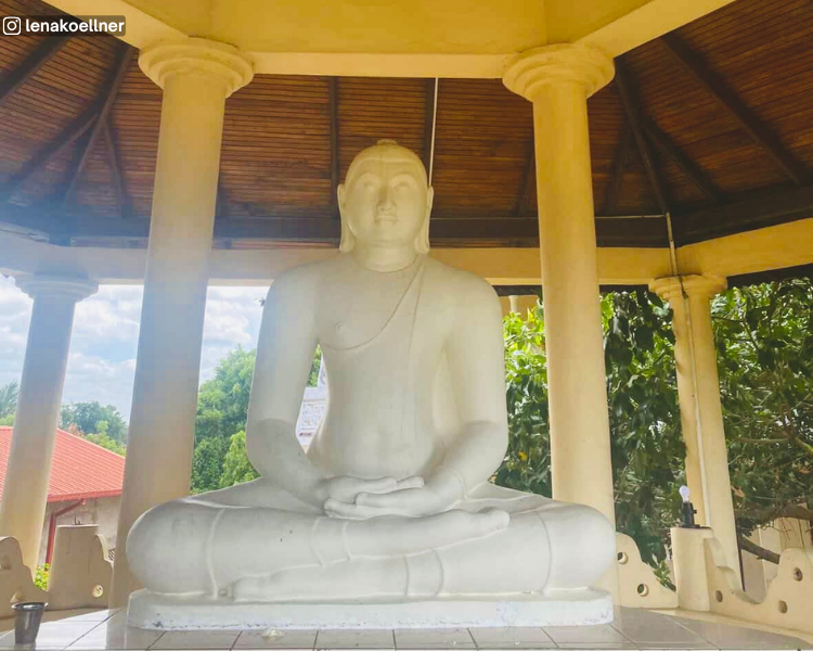 White Buddha statue beneath a shrine roof at Muhudu Maha Viharaya near Pottuvil, Sri Lanka