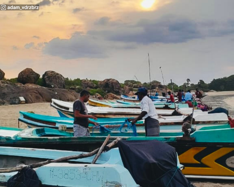 Fishing boats lined along the beach beside a rocky shoreline at Pottuvil Beach near Arugam Bay, Sri Lanka
