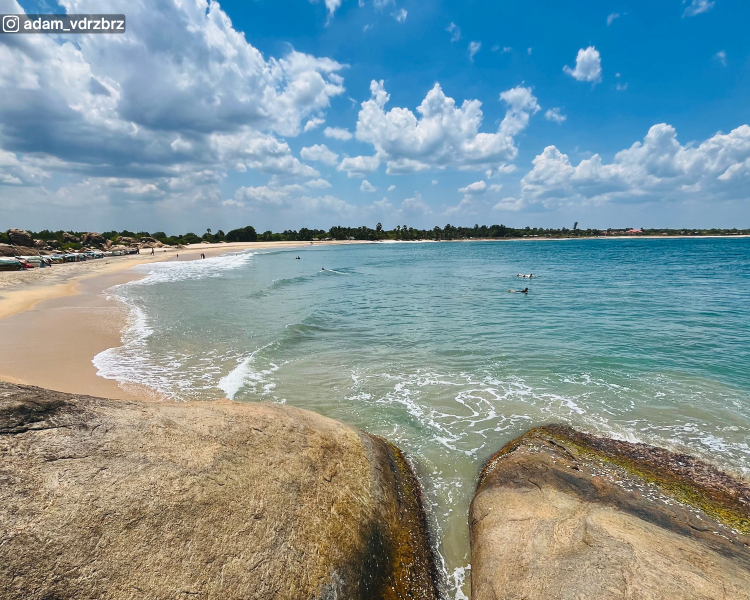 Sea view with surfers, rocky shore and distant tree line at Pottuvil Point near Arugam Bay, Sri Lanka