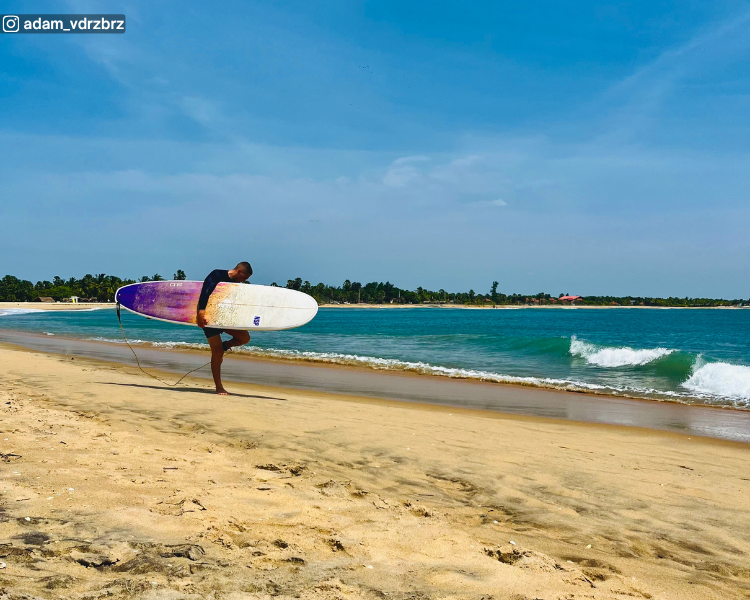 Surfer holding a board with the sea behind him at Pottuvil Point near Arugam Bay, Sri Lanka
