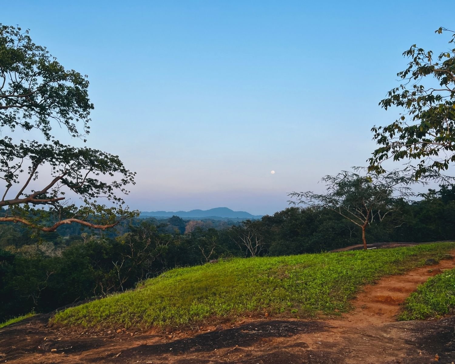 Full moon rising over distant hills from grassy mid-tier plateau with red earth path at Mapagala Fortress Little Pidurangala Sri Lanka
