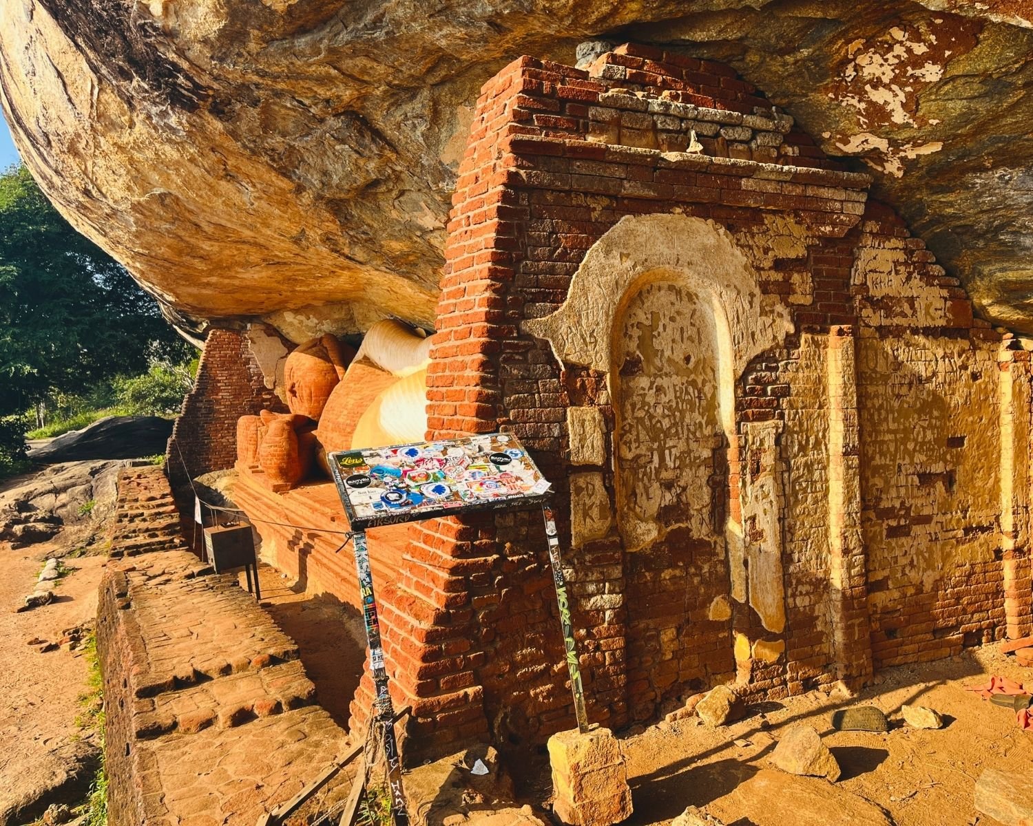 Reclining Buddha statue inside brick cave shrine under massive rock overhang at Pidurangala Raja Maha Viharaya near Sigiriya