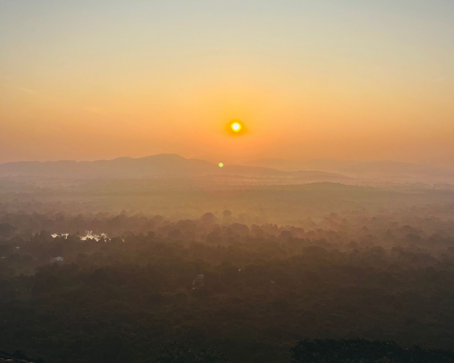 Sunrise over misty jungle valleys and layered mountains with small lake, view east from Pidurangala Rock summit near Sigiriya