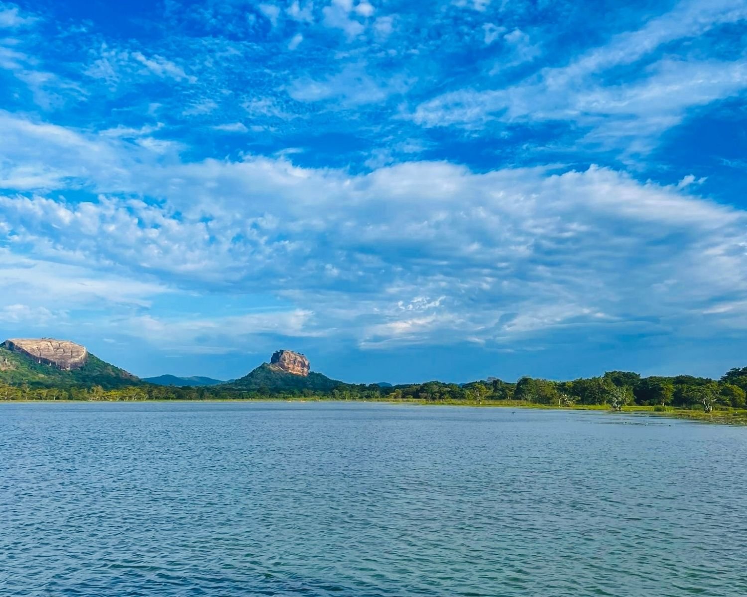 Thalkote Wewa ancient irrigation reservoir with Pidurangala Rock left and Lion Rock right under dramatic blue sky with clouds near Sigiriya
