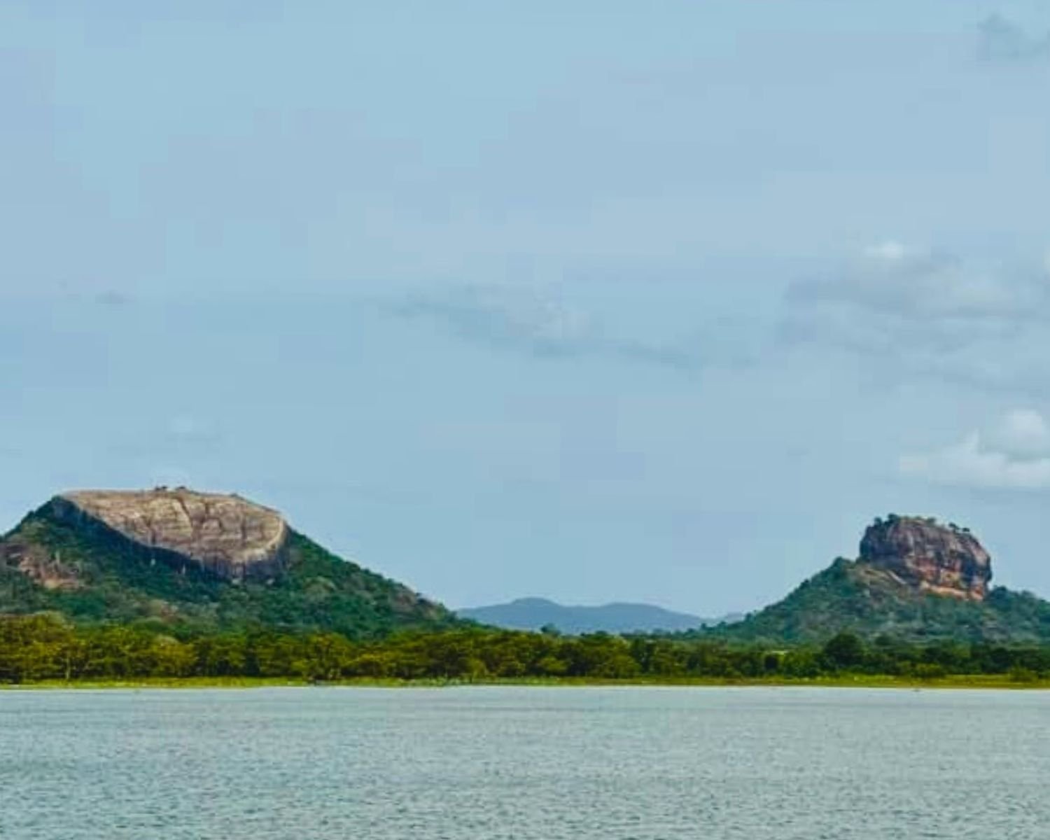 Telephoto view across Thalkote Wewa ancient irrigation reservoir to Pidurangala Rock left and Lion Rock right with hazy sky near Sigiriya