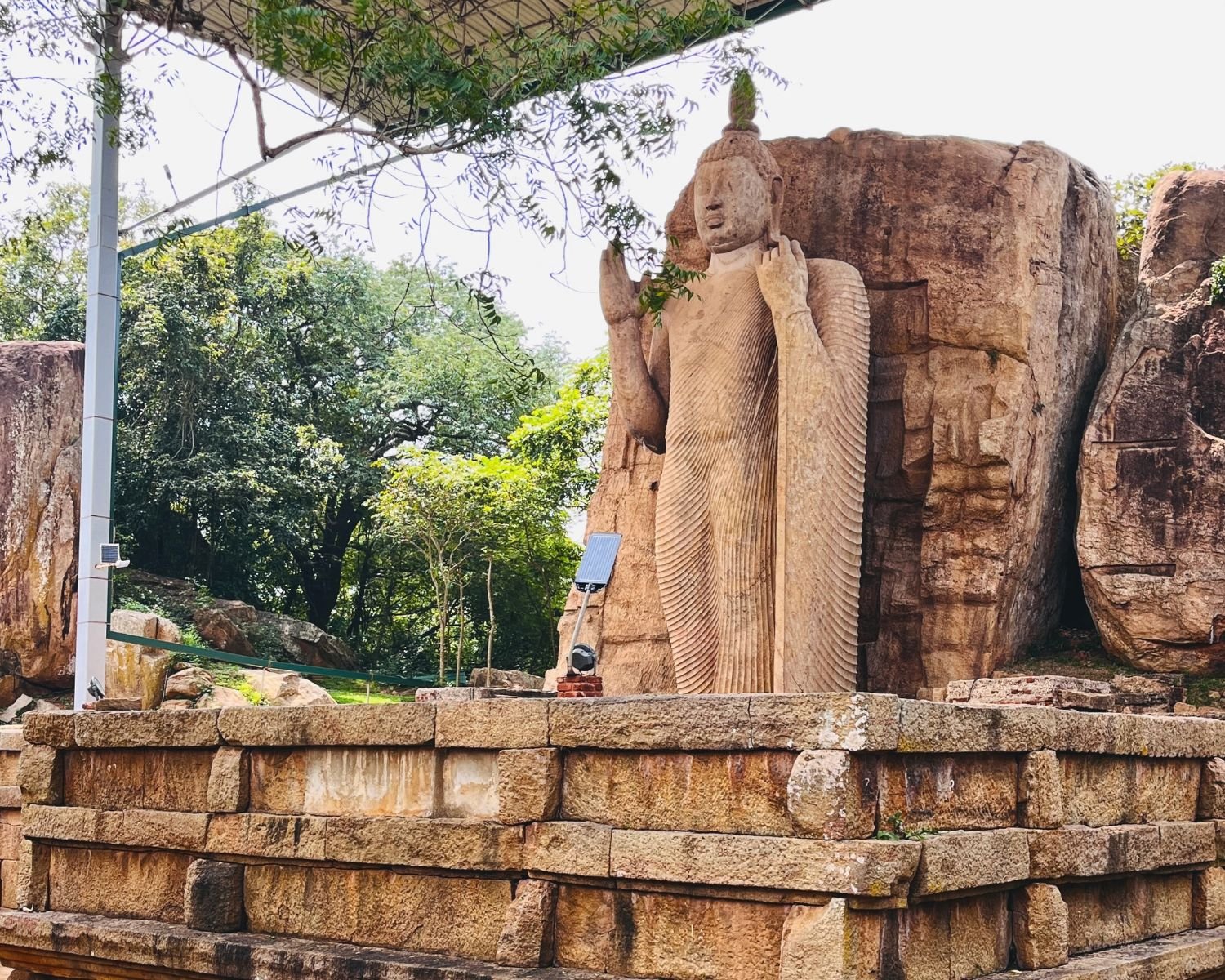 Ancient Aukana Buddha Statue standing beside a forested rock outcrop