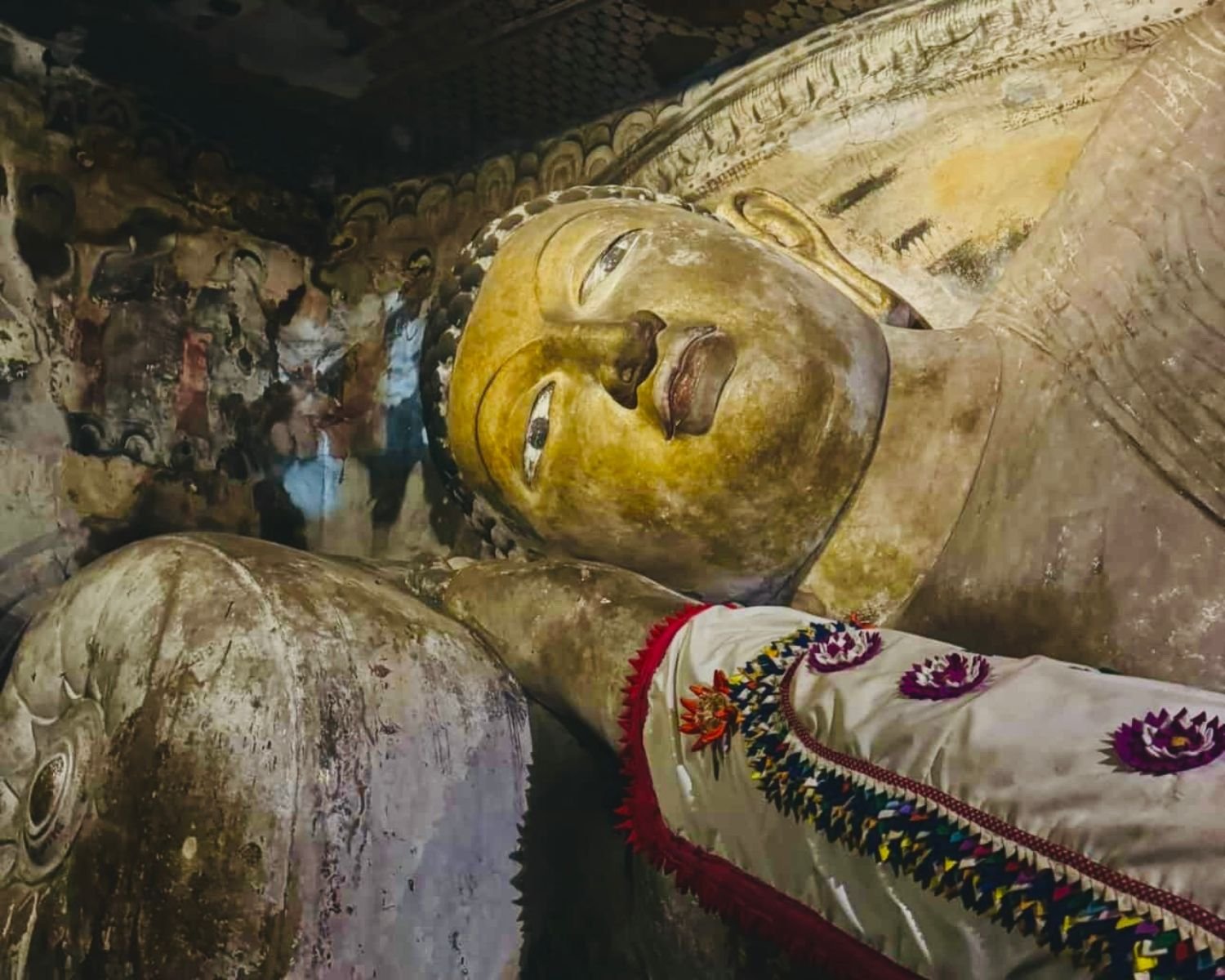Face of the reclining Buddha with painted cave murals behind