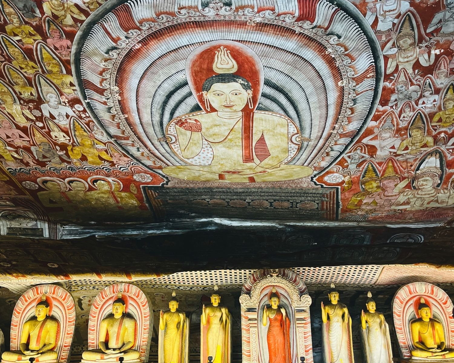 Colourful painted rock ceiling with Buddha and deity murals above shrine statues
