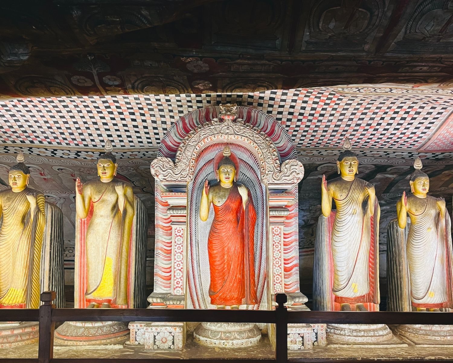 Buddha statues beneath red and black patterned ceiling murals