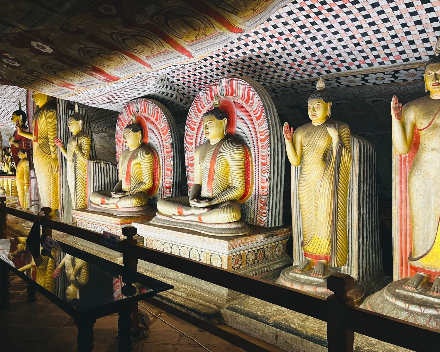 Seated and standing Buddha statues beneath chequered ceiling murals