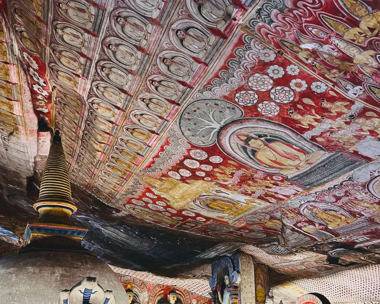 Painted rock ceiling with Buddha images, deity figures, and a stupa below
