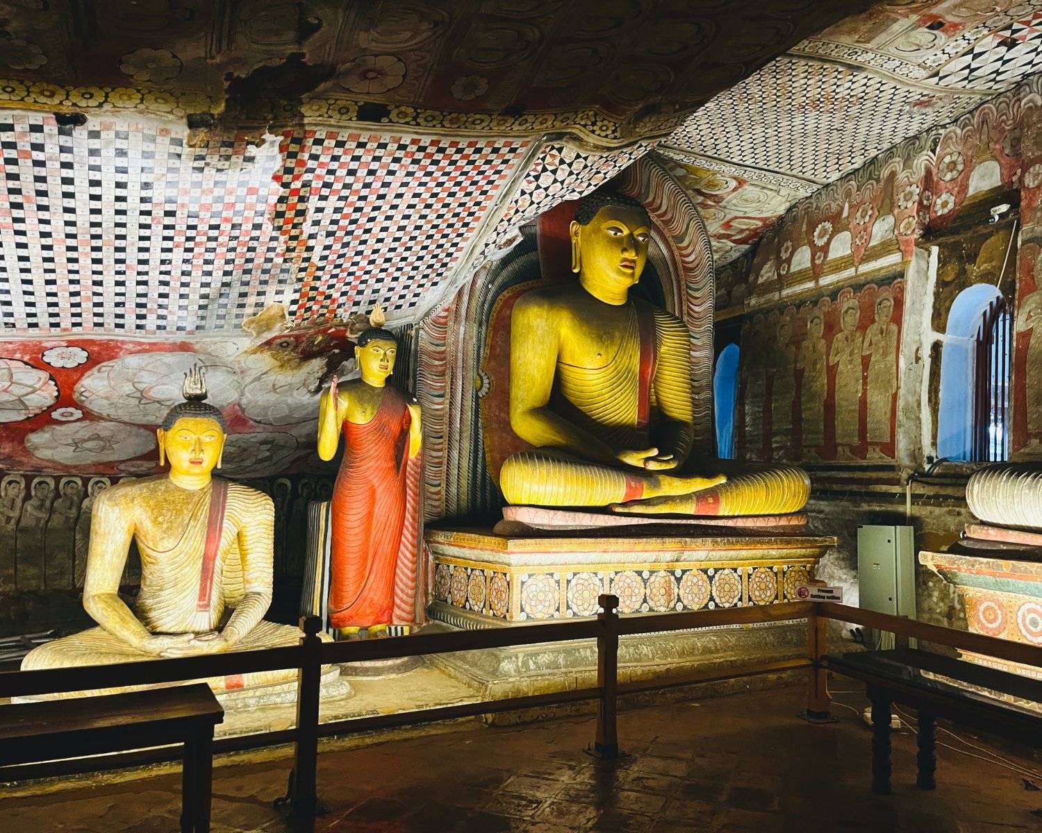 Seated Buddha statue beneath patterned cave ceiling murals