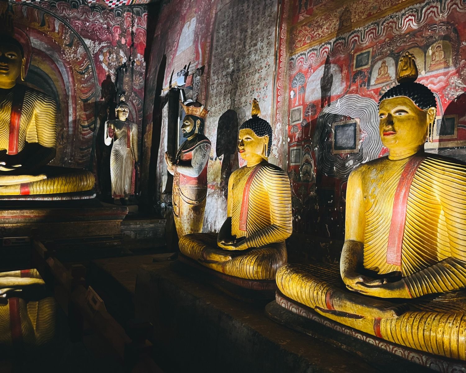 Seated Buddha statues with Kandyan-era murals and a royal statue