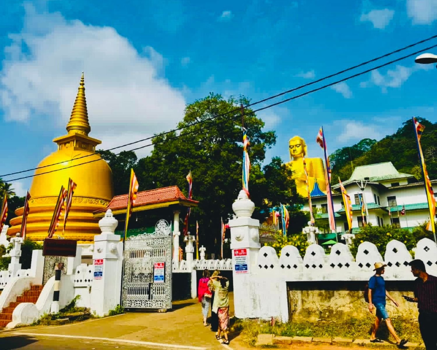 Golden stupa, large Buddha statue, and Buddhist flags at the temple entrance