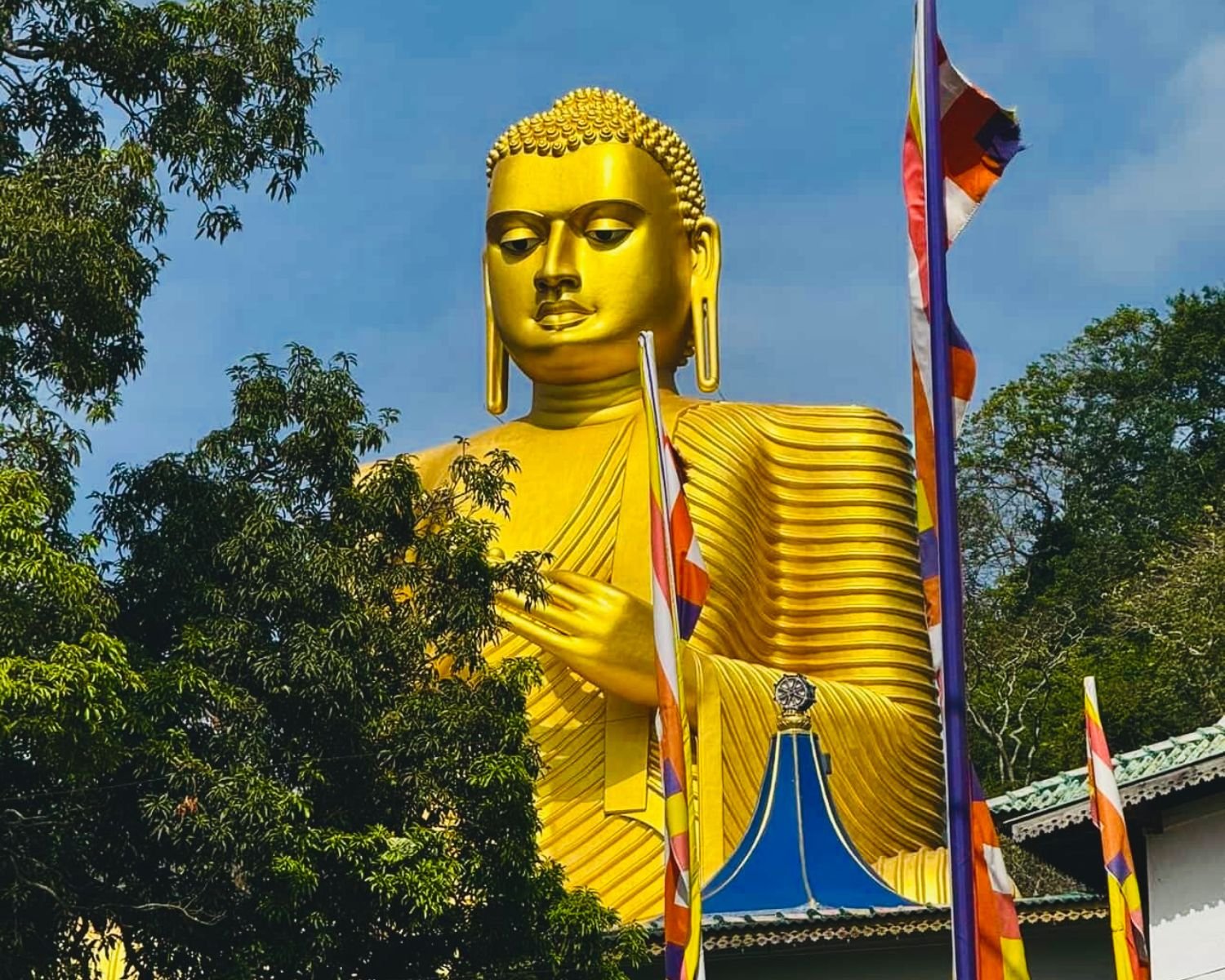 Giant golden Buddha statue framed by trees and Buddhist flags