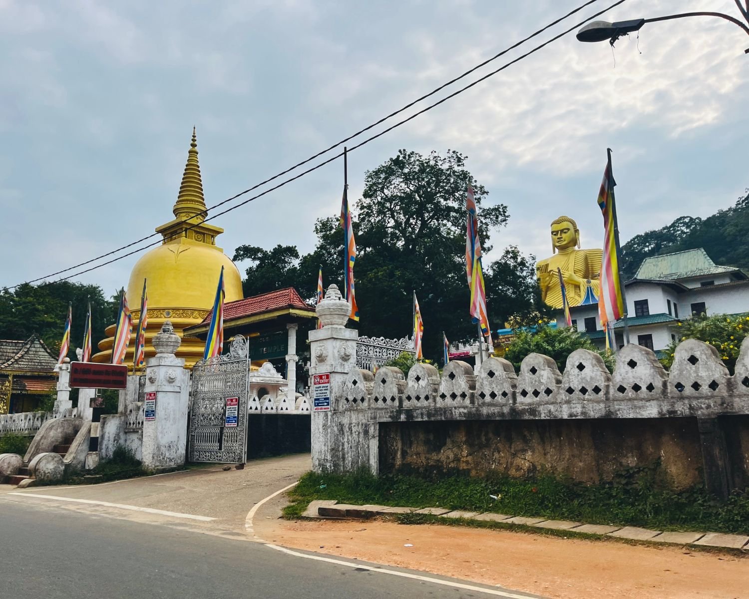 Roadside view with golden stupa, Buddha statue, and white boundary wall