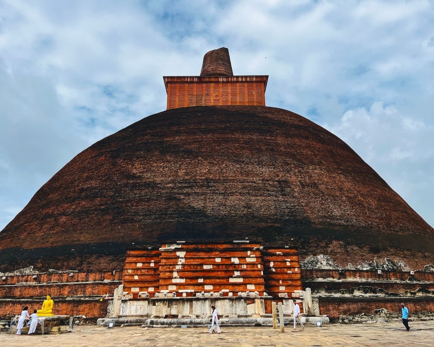 Jetavanaramaya east face with brick dome, square harmika, vahalkada frontispiece, and yellow Buddha statue on stone courtyard