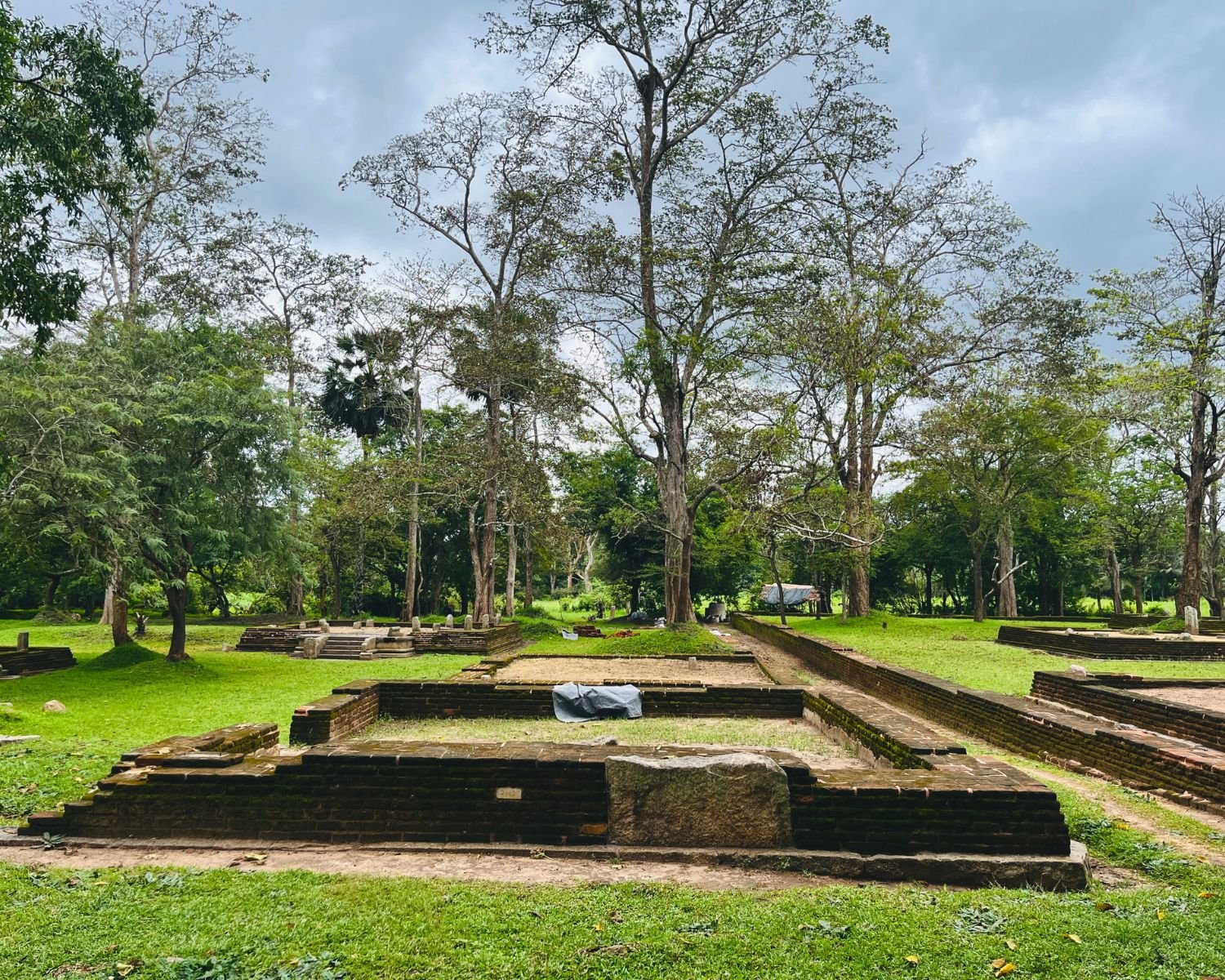 Ancient monk residence ruins at Jetavanaramaya with brick foundations, stone platforms, and trees in monastic park