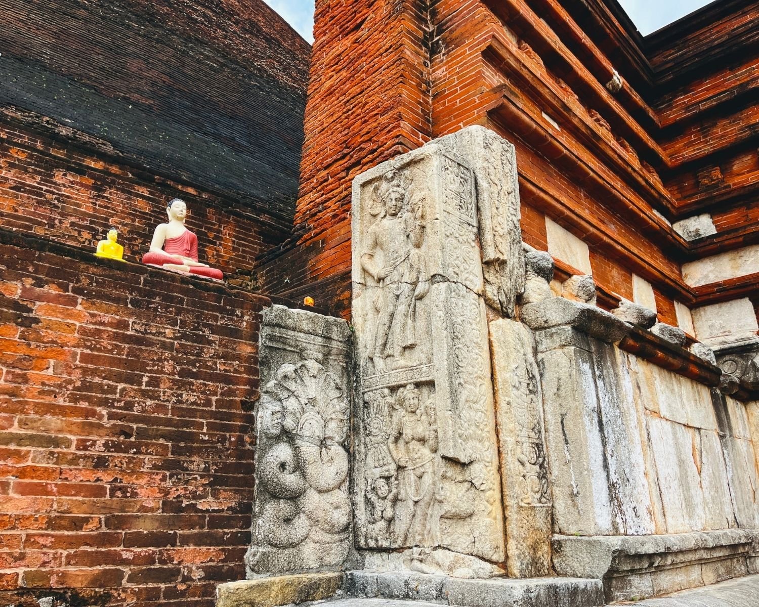 Jetavanaramaya west vahalkada corner with carved stone guardstone, naga sculpture, and Buddha statues on brick wall