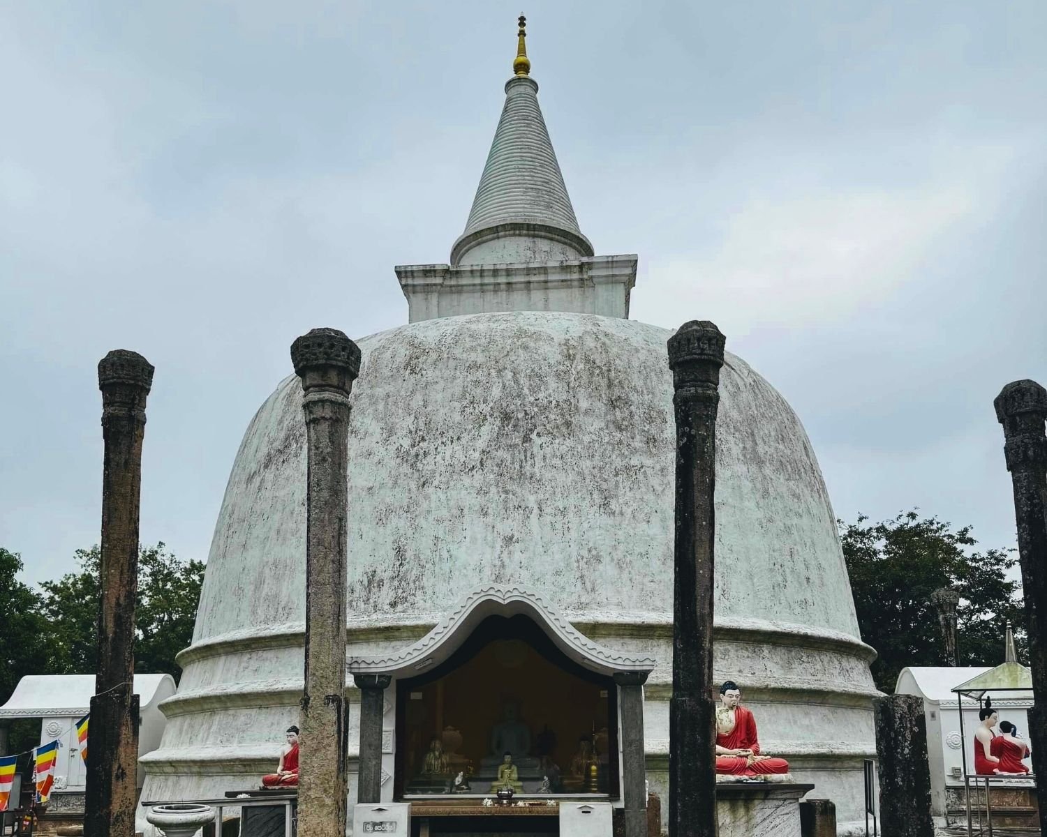 Front view of Lankarama white stupa with carved stone pillars, golden spire, and glass Buddha shrine at Anuradhapura