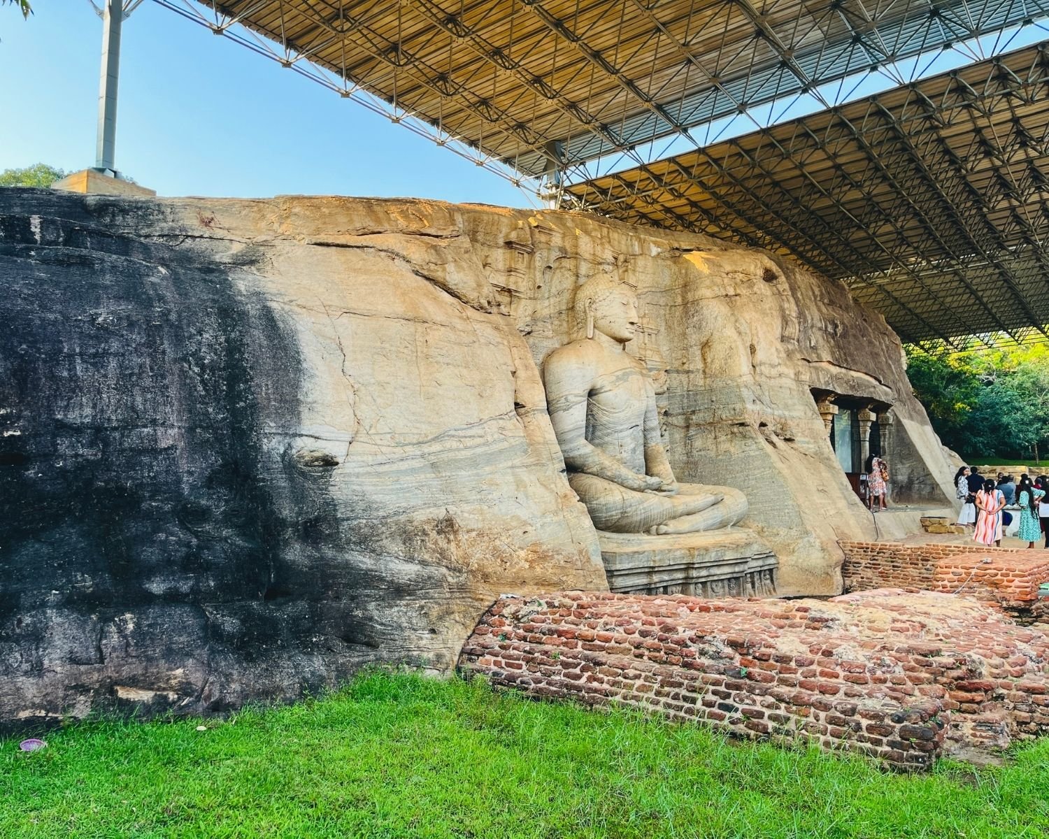 Side view of seated Buddha at Gal Vihara with brick foundation ruins in foreground