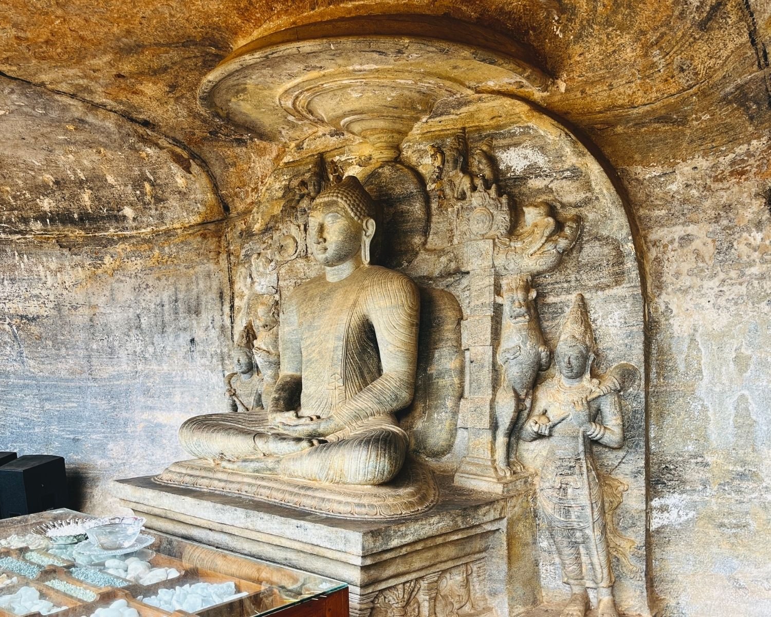 Small seated Buddha inside rock-cut niche with guardian figures at Gal Vihara Uttararama