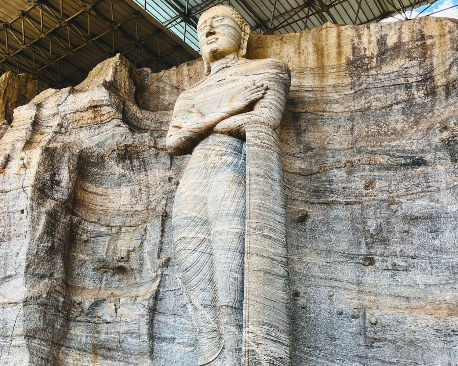 Standing Buddha with crossed arms and detailed robe lines at Gal Vihara Uttararama