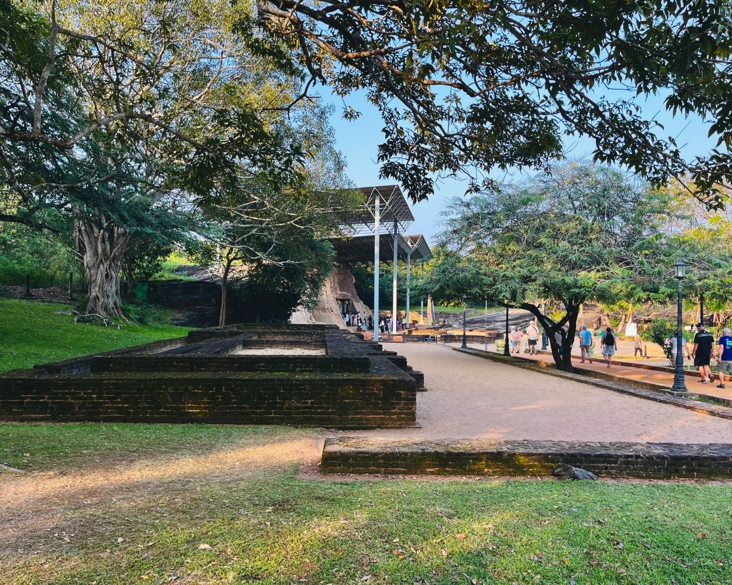 Visitor path and brick foundation ruins with seated Buddha in distance at Gal Vihara