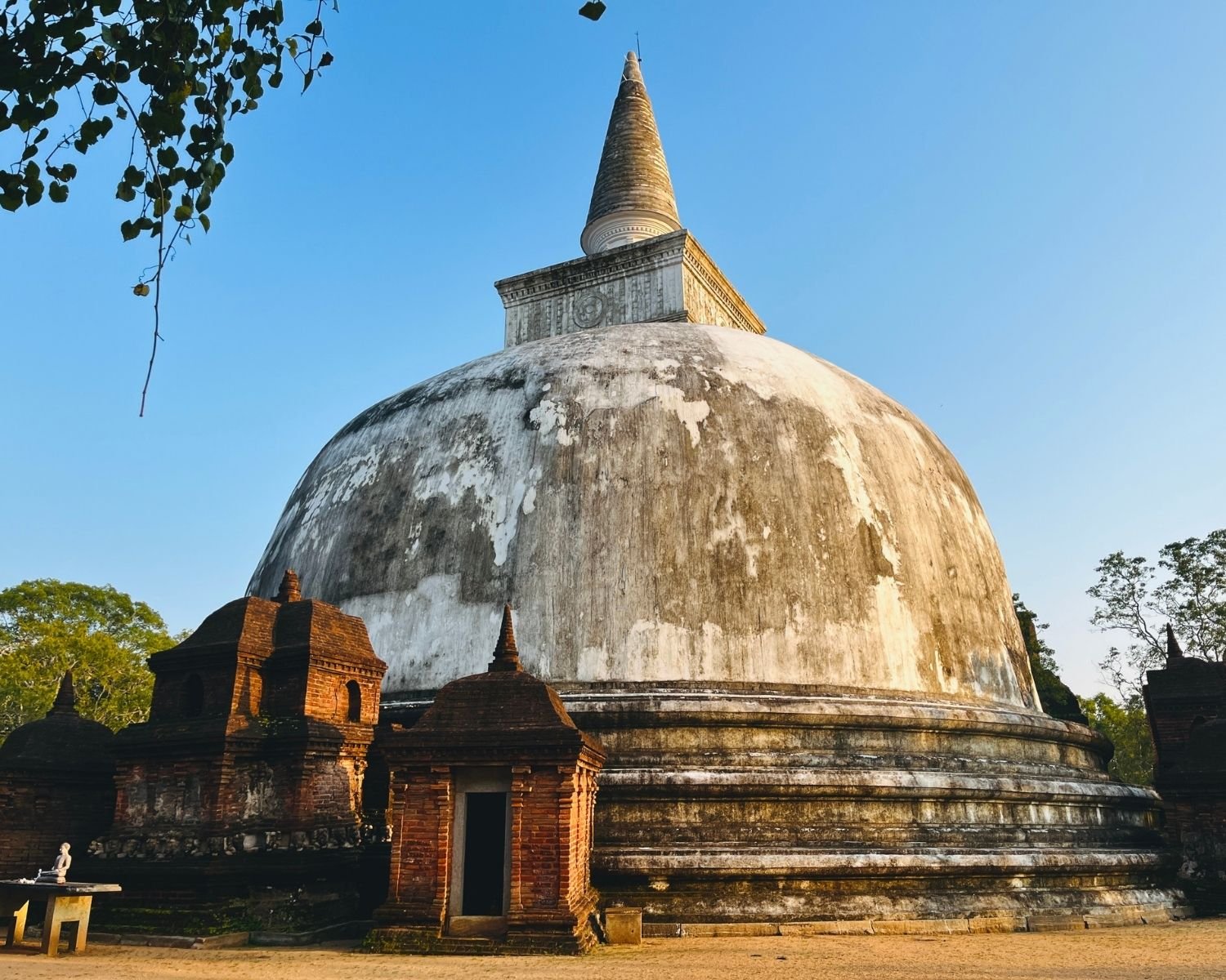 Kiri Vehera white dagoba with restored spire and brick vahalkada frontispieces framed by Bodhi tree branches