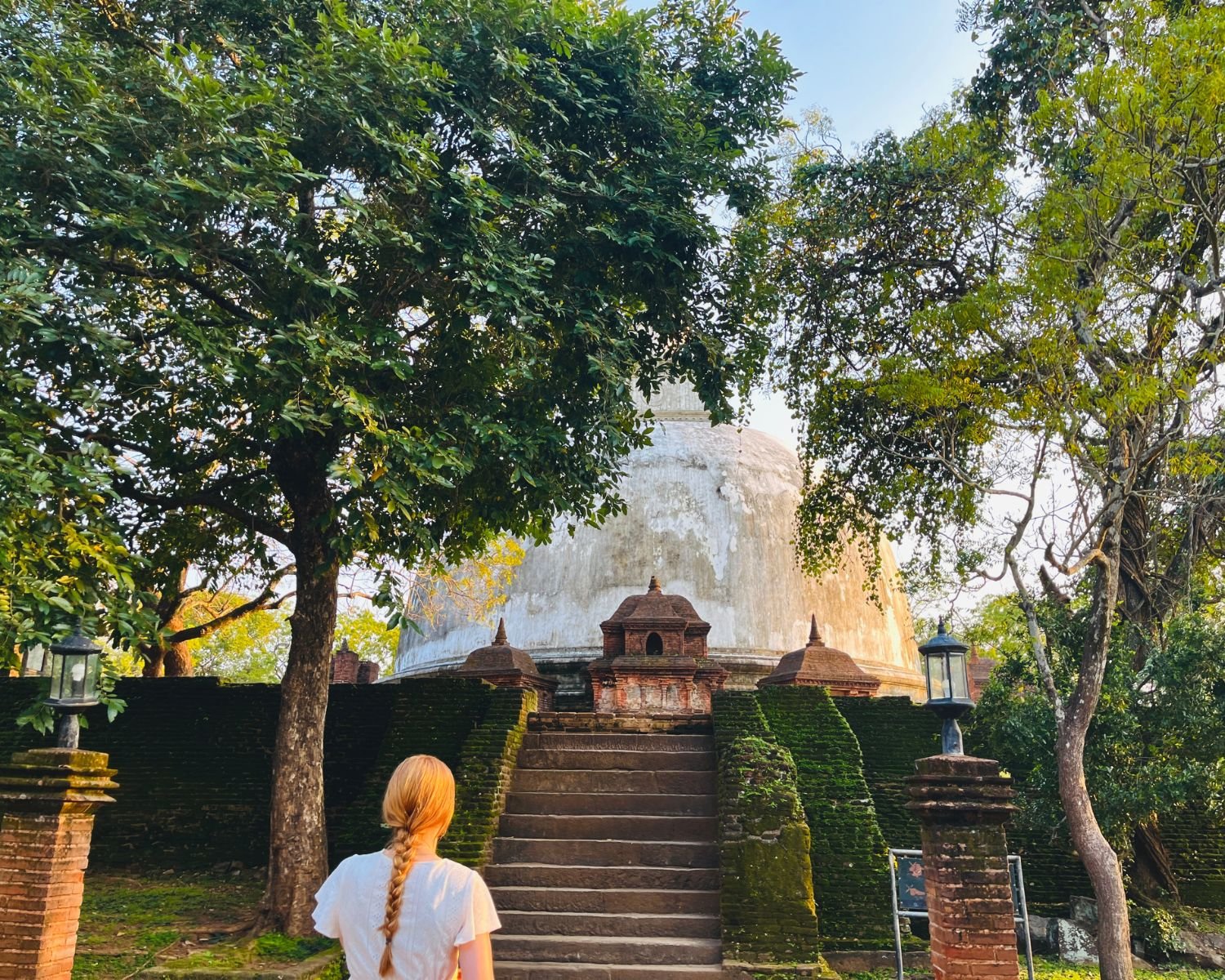 Stone staircase and mossy brick walls leading to brick shrines at base of Kiri Vehera stupa at sunset