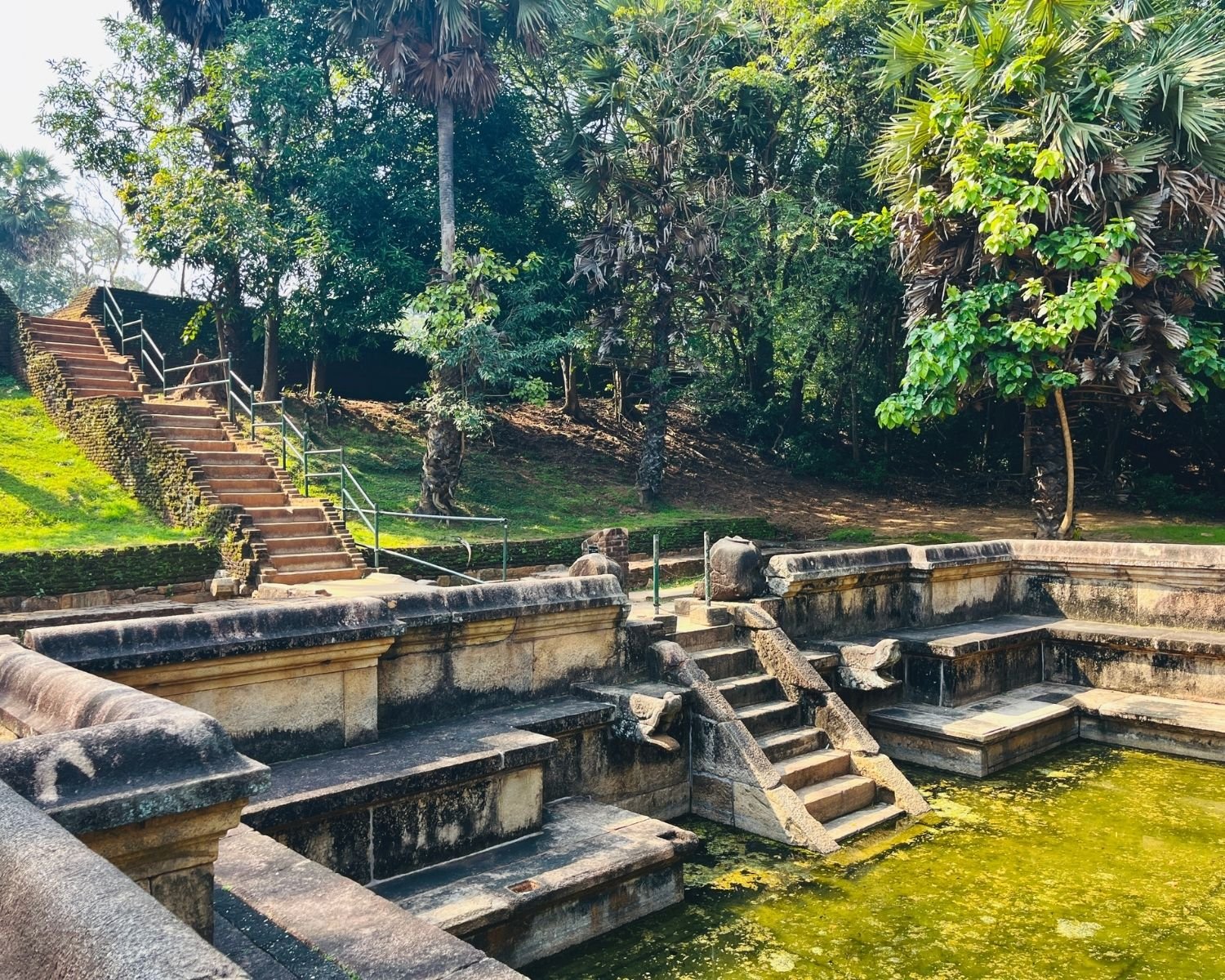 Side view of Kumara Pokuna showing stone steps, inner ledges, carved details, and pond basin