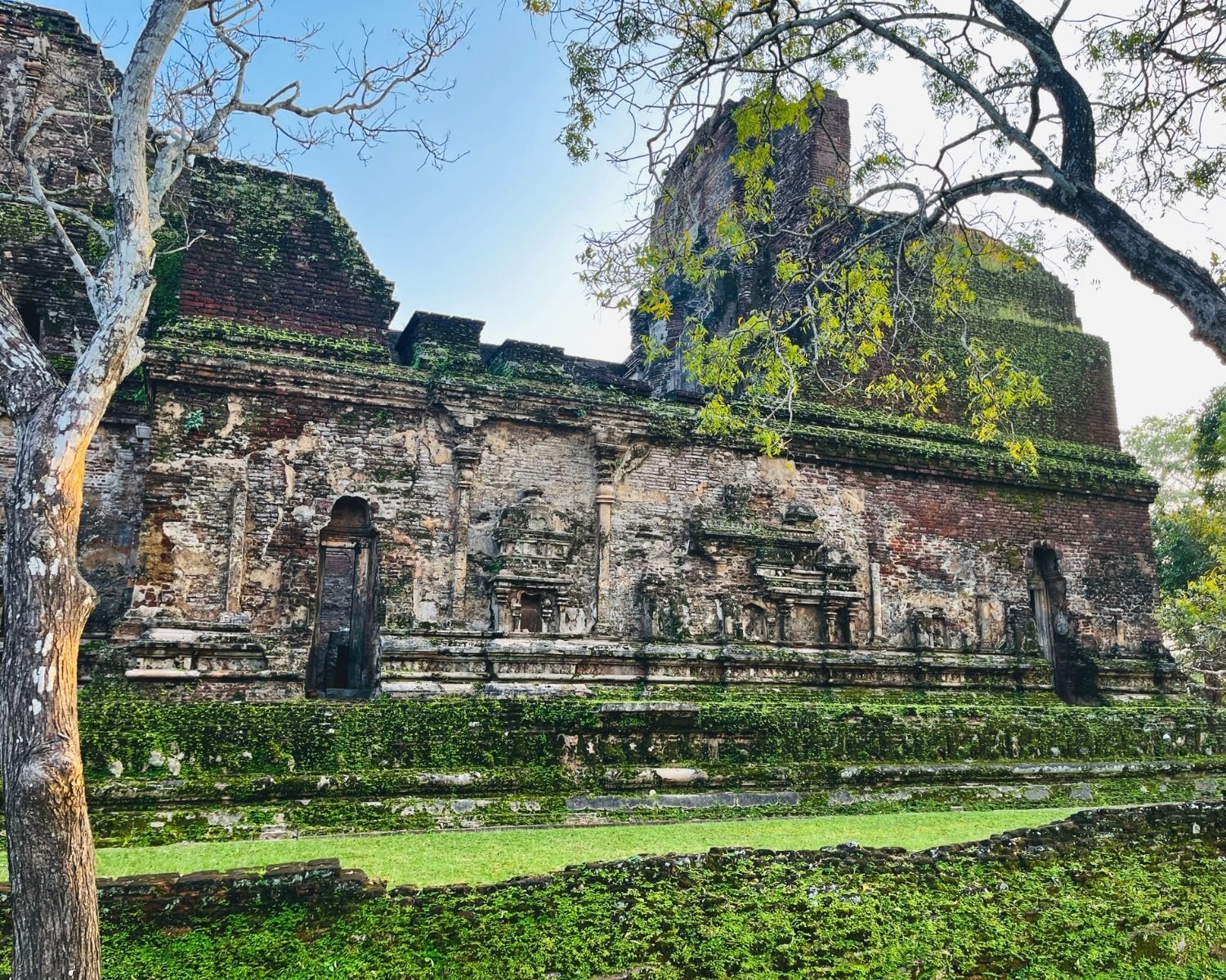 Moss-covered north wall of Lankatilaka with two false door niches and stucco reliefs between brick sections