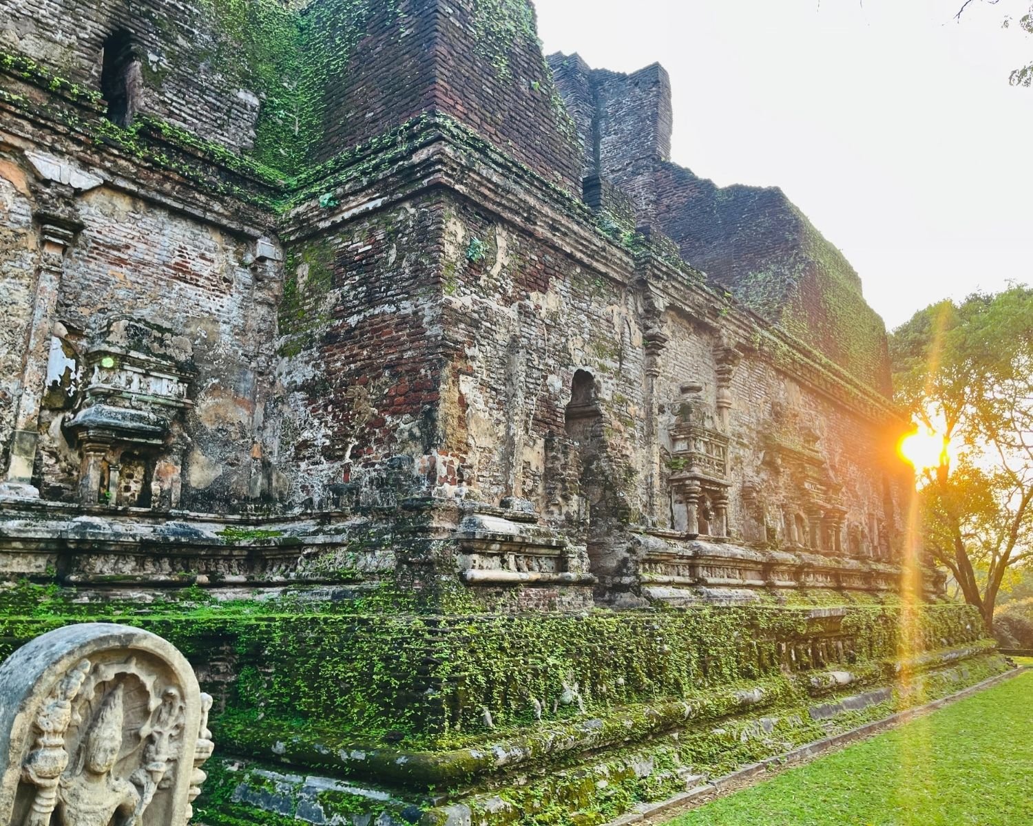 Western end of Lankatilaka north wall at sunset showing brick corner, arched niche, and moss-covered base
