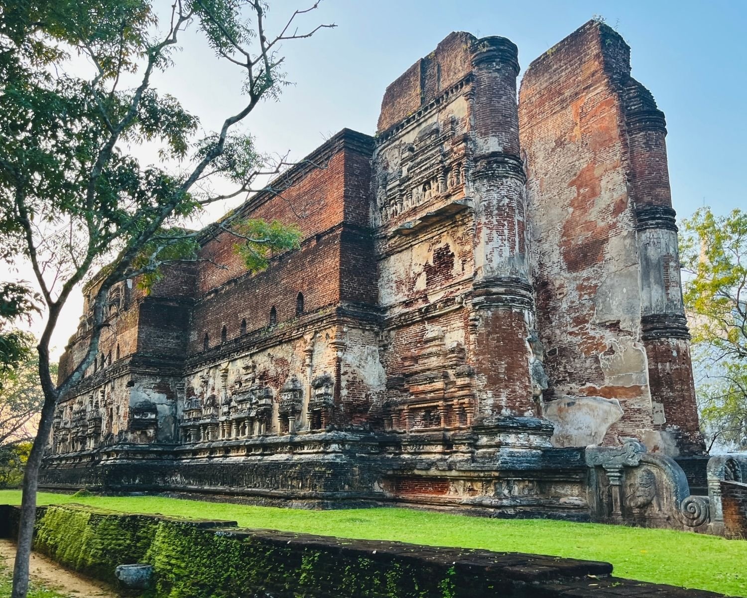 South wall and southeast corner of Lankatilaka with brick facade, miniature shrine reliefs, and moonstone at east entrance